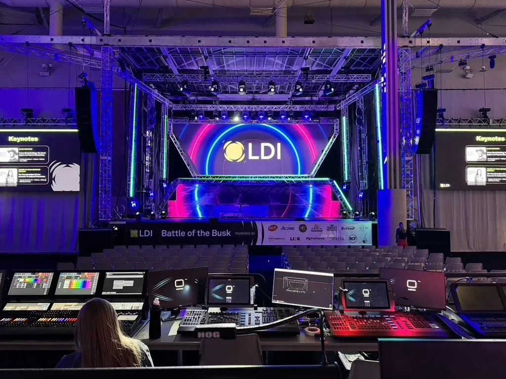 Empty conference hall with stage equipped with lighting, large screens, and LED displays. A control panel with audio and visual equipment in the foreground. The event is titled "Battle of the Busk" with branding for LDI.