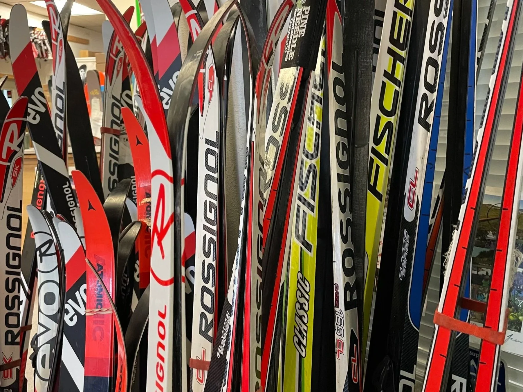 Ski equipment hanging on a rack, including skis, poles, and gloves, with a snowy outdoor background.