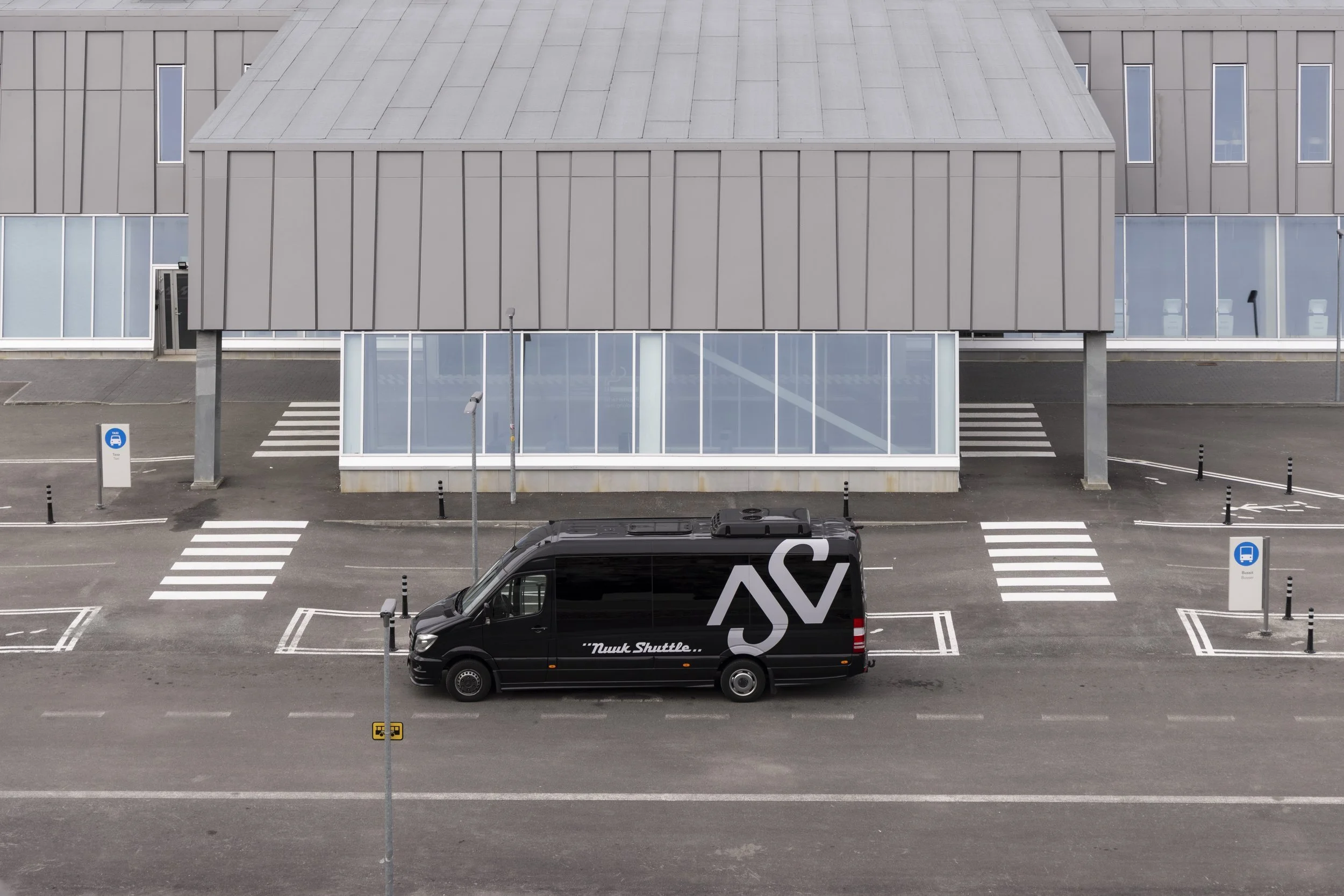 Empty parking lot with a black shuttle van labeled 'Nuuk Shuttle' parked near Nuuk International Airport.