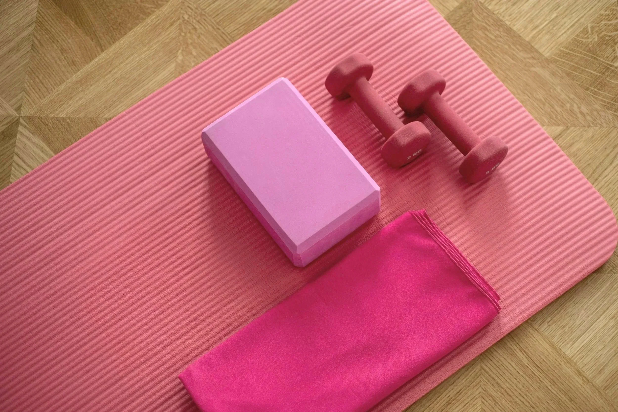 Pink yoga mat with pink dumbbells, foam block, and pink resistance band.