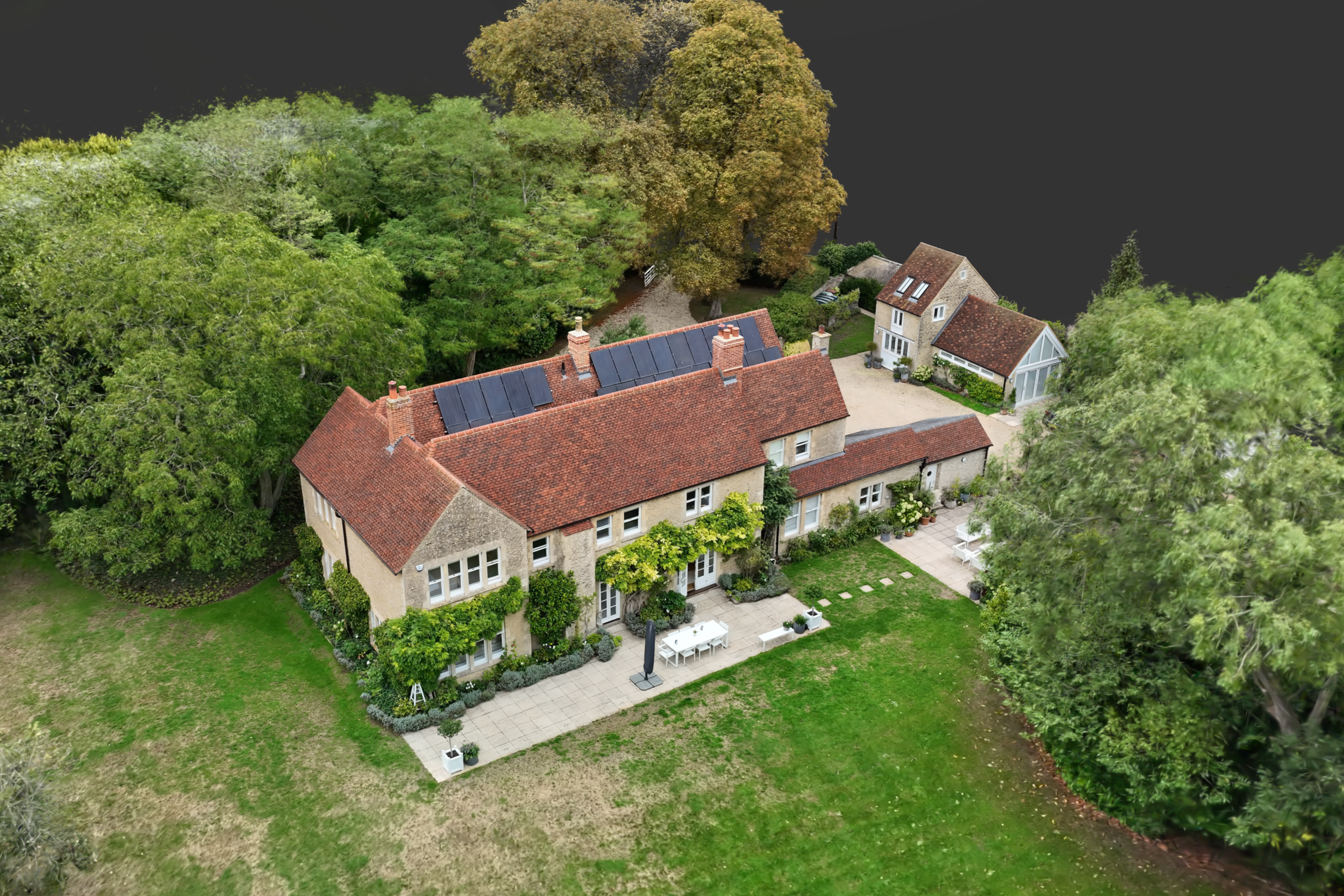 An aerial view of an old stone tower with a tall chimney, surrounded by grassy paths and shrubbery.