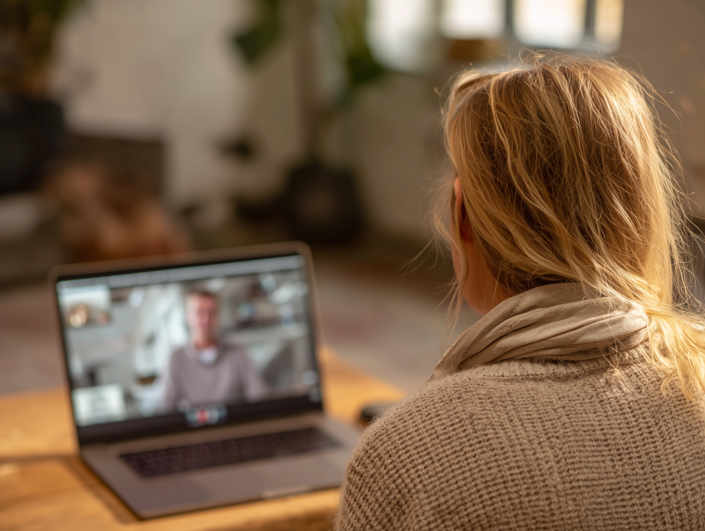 En person med blondt hår ikledd en beige genser og en lys skjerf, som sitter foran en bærbar PC