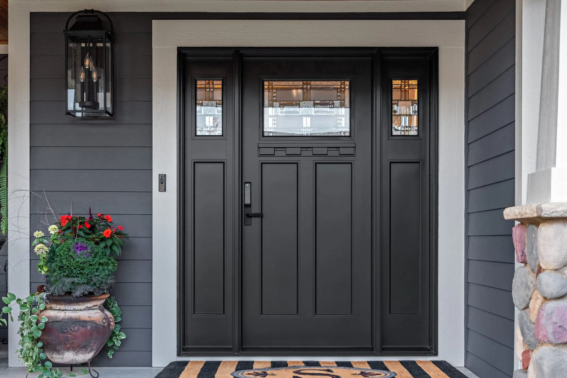 Black entry door with sidelights, installed with stone and floral accents – Raleigh Entryworks project.