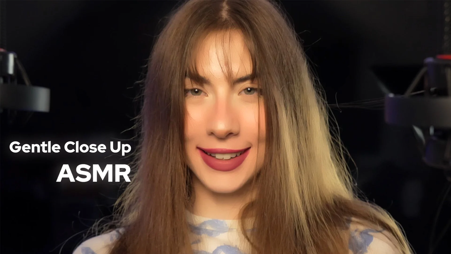 A young woman with long, light brown hair smiling gently with closed lips, in front of a black background with camera equipment visible. Overlay text reads "Gentle Close Up ASMR".