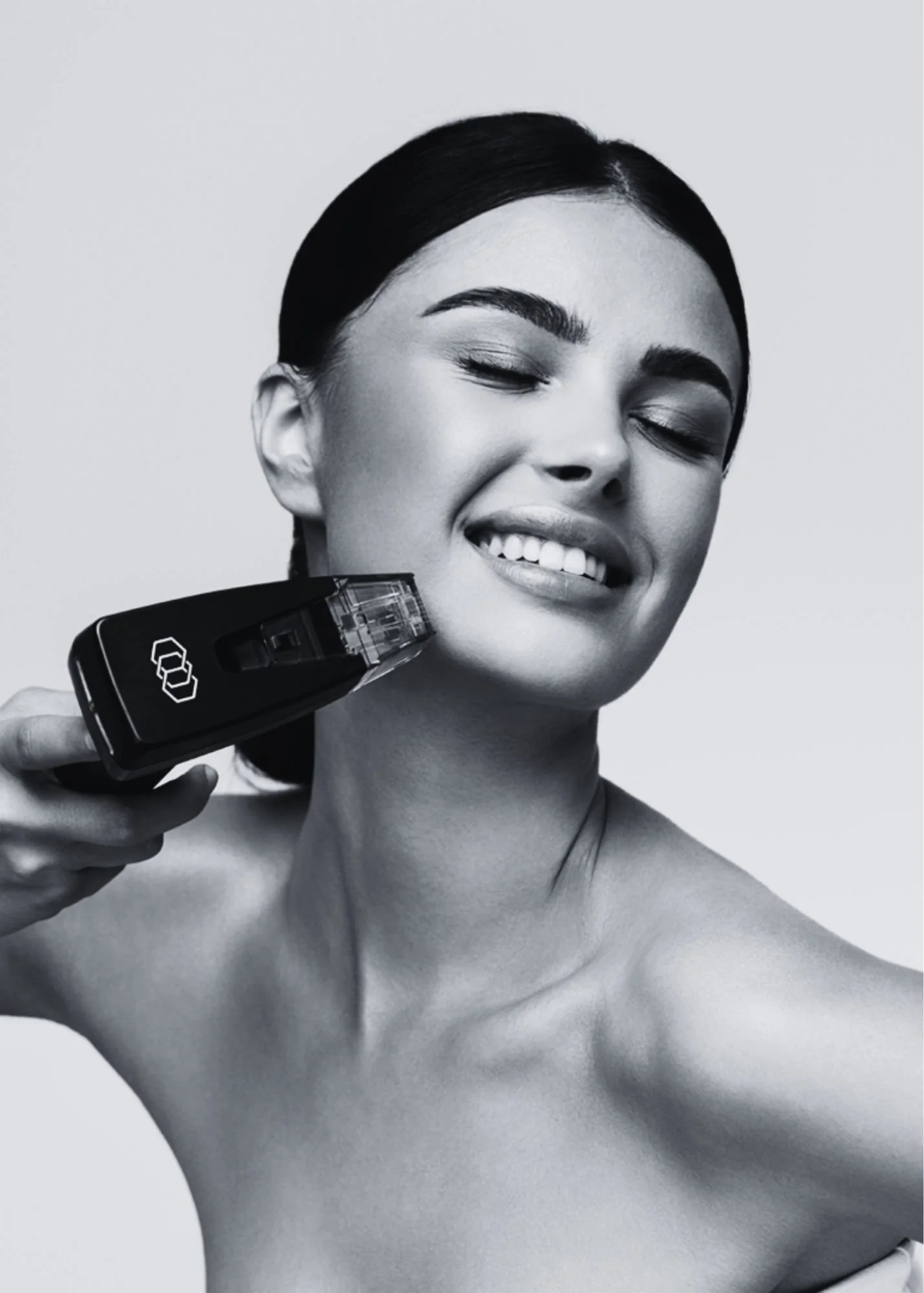 A woman with dark hair and makeup smiling as she uses an electric shaver on her neck.