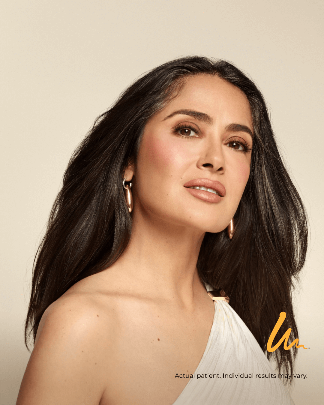 Portrait of a woman with long dark hair, wearing earrings, and a white top against a neutral background.