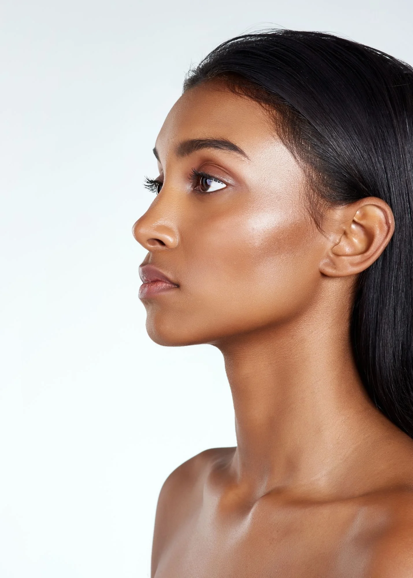 Profile of a young woman with medium brown skin, straight black hair, and natural makeup, looking to the left against a plain light background.