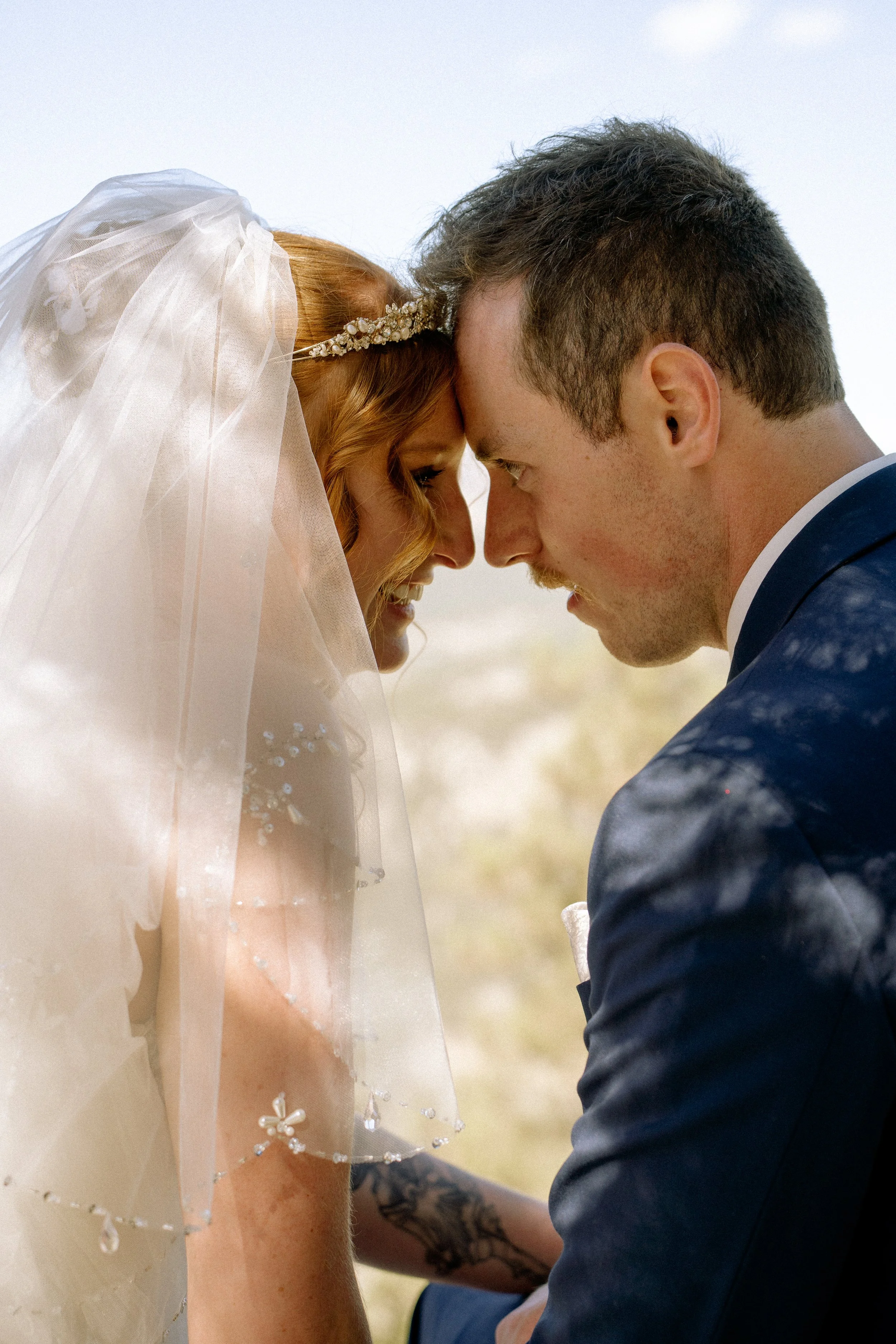 Close-up of a bride and groom touching foreheads, smiling, during their wedding outdoor ceremony.