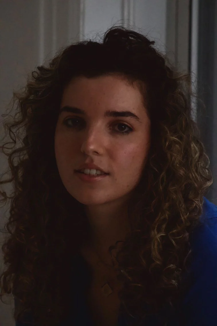 An image of white woman with curly hair and a blue sweater looking into the camera