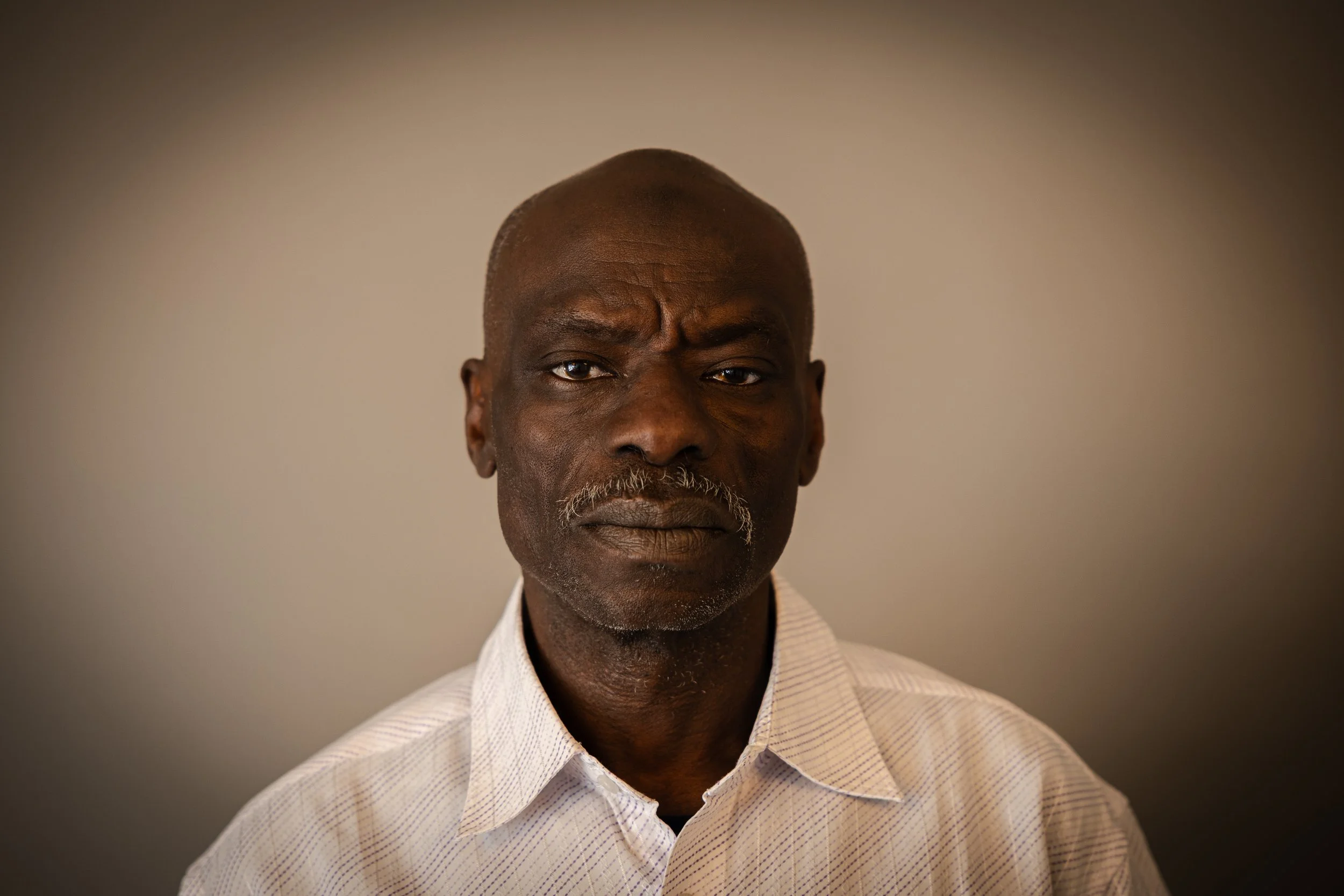 Portrait of a middle-aged Black man with a serious expression, wearing a white collared shirt against a plain background.