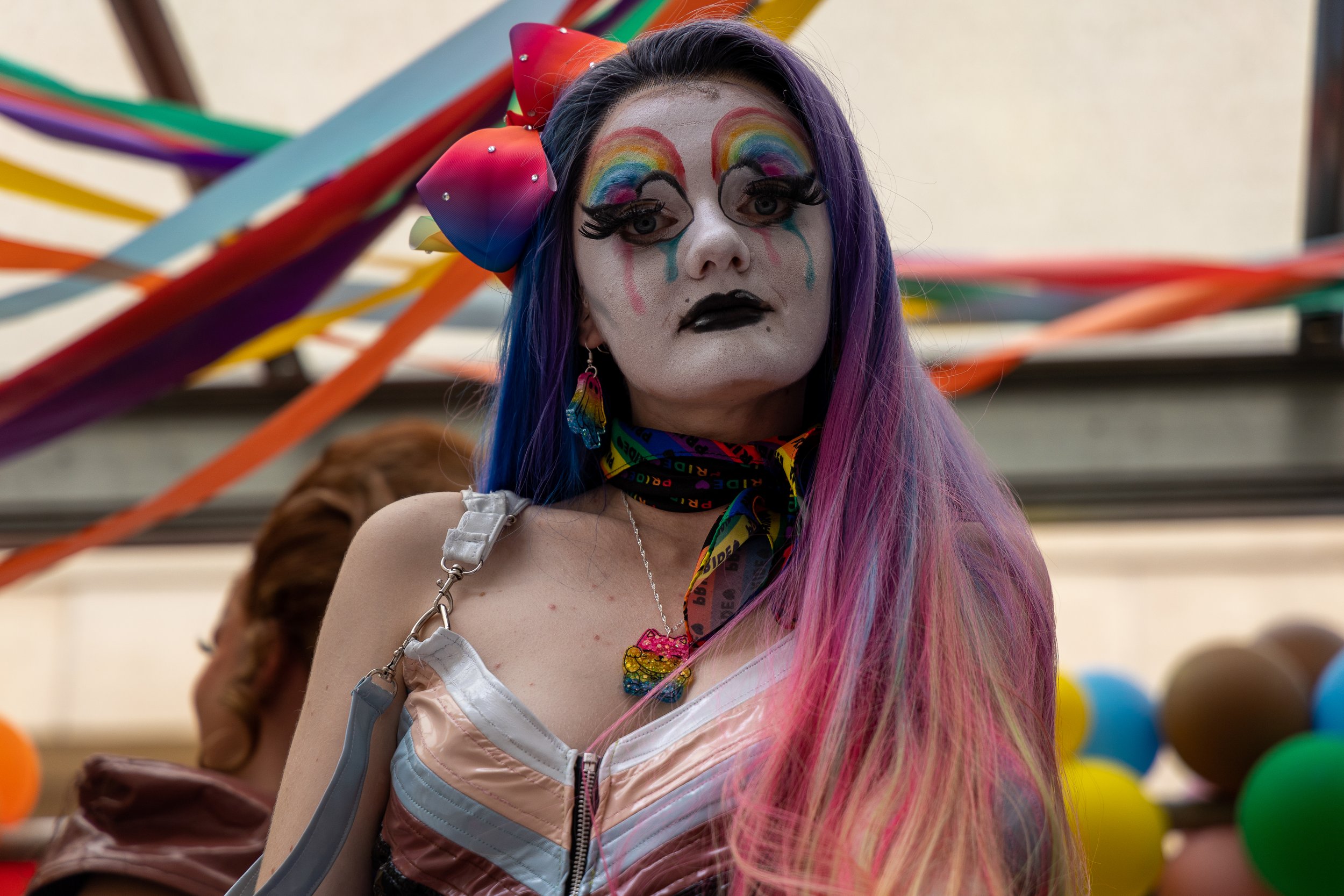 Person with rainbow-colored hair, dramatic makeup, and rainbow-themed jewelry at a colorful event.