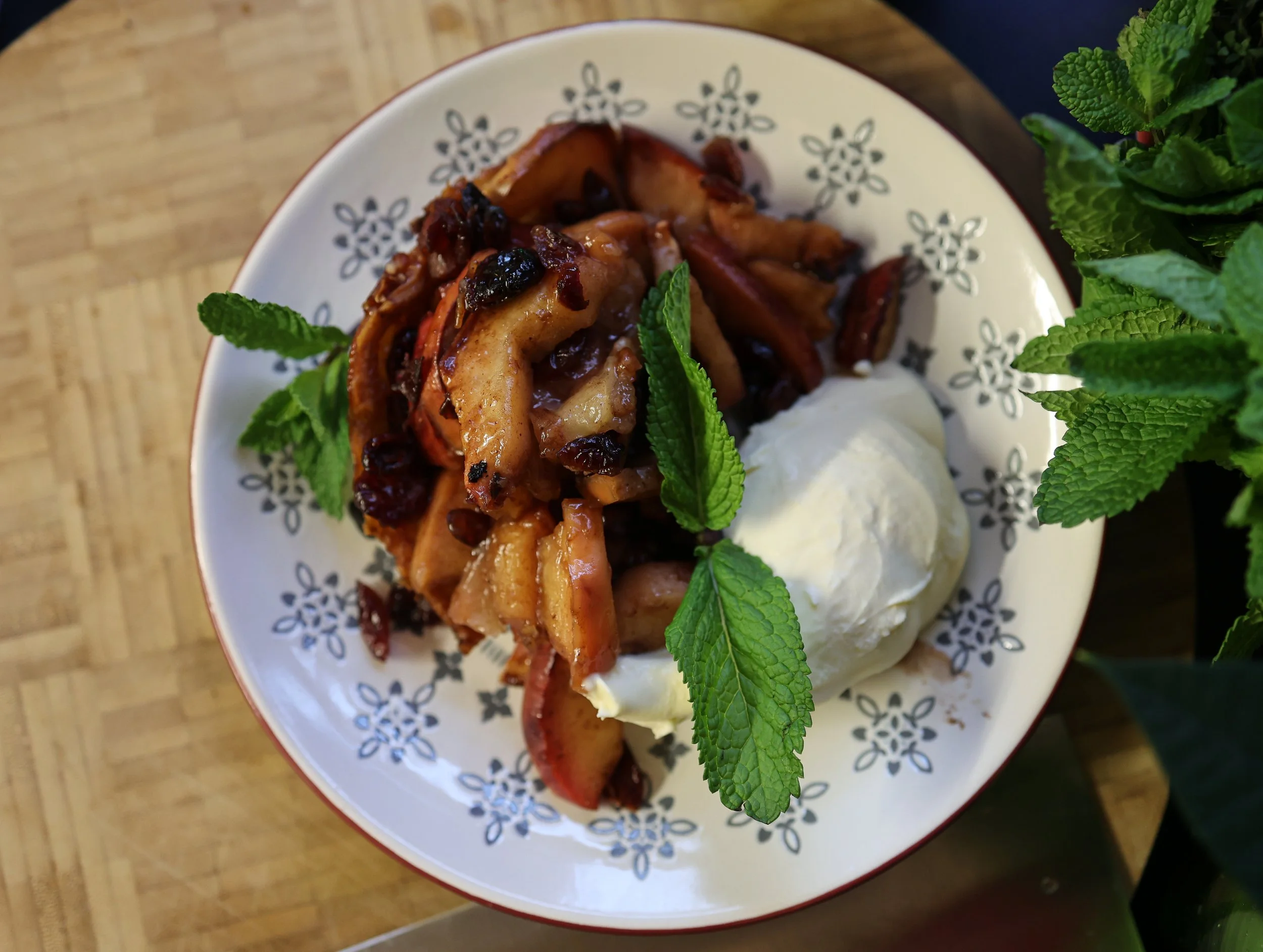A plate of apple cobbler with vanilla ice cream and fresh mint leaves on top