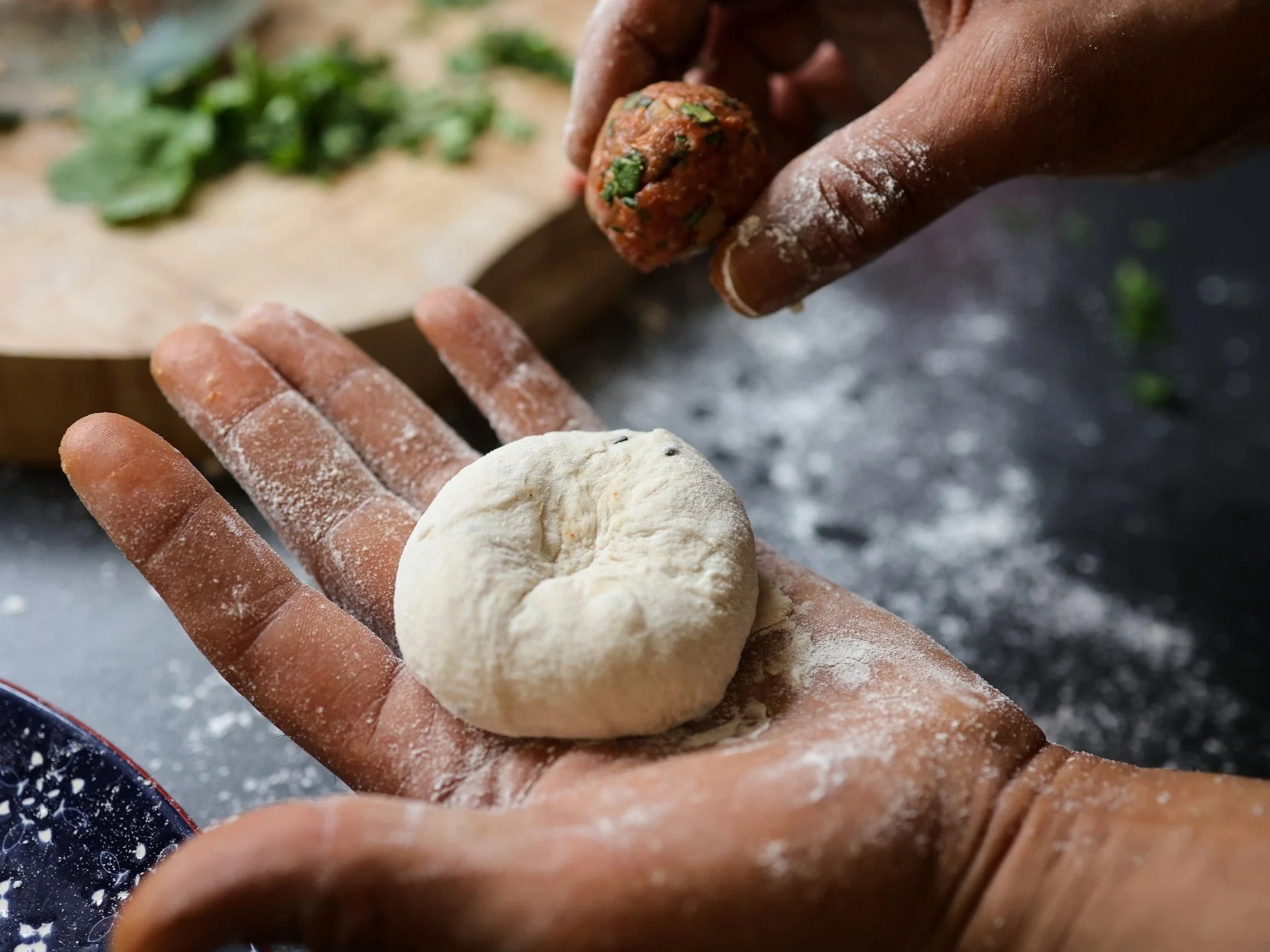 Hands forming an uncooked bread or dough ball, with a ball of spiced meat or vegetable filling above