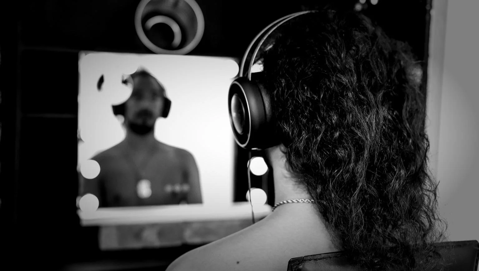 A woman with curly hair wearing headphones in a recording or photography studio, looking at a screen wearing headphones