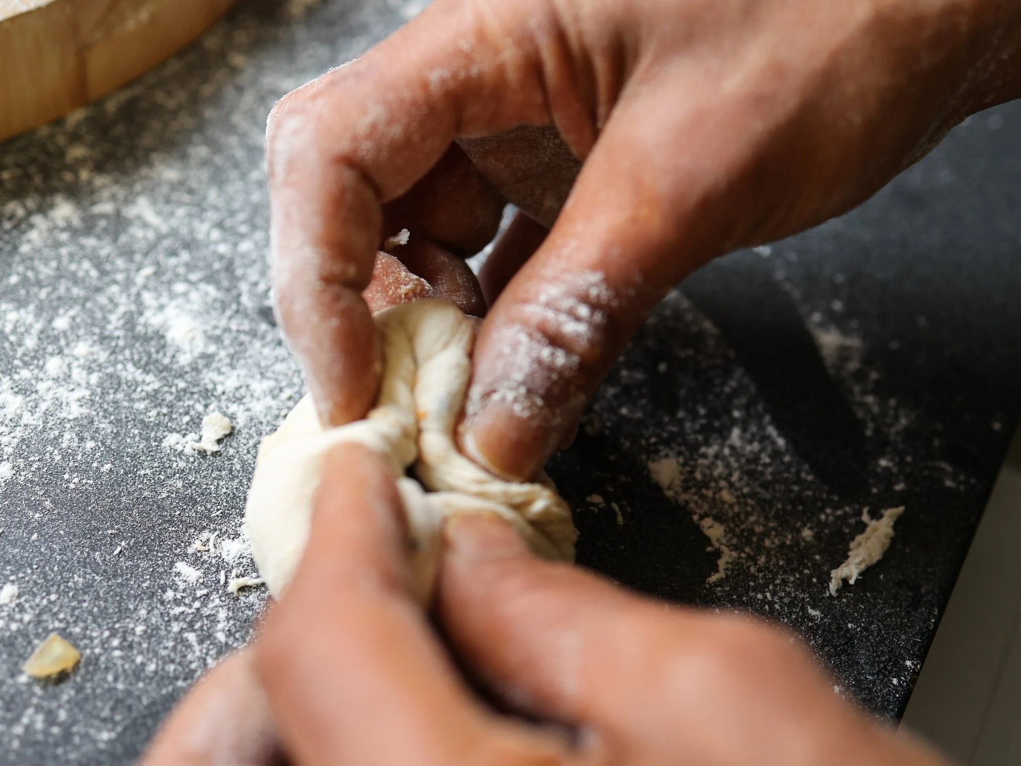 Person folding and shaping dough on a floured surface.