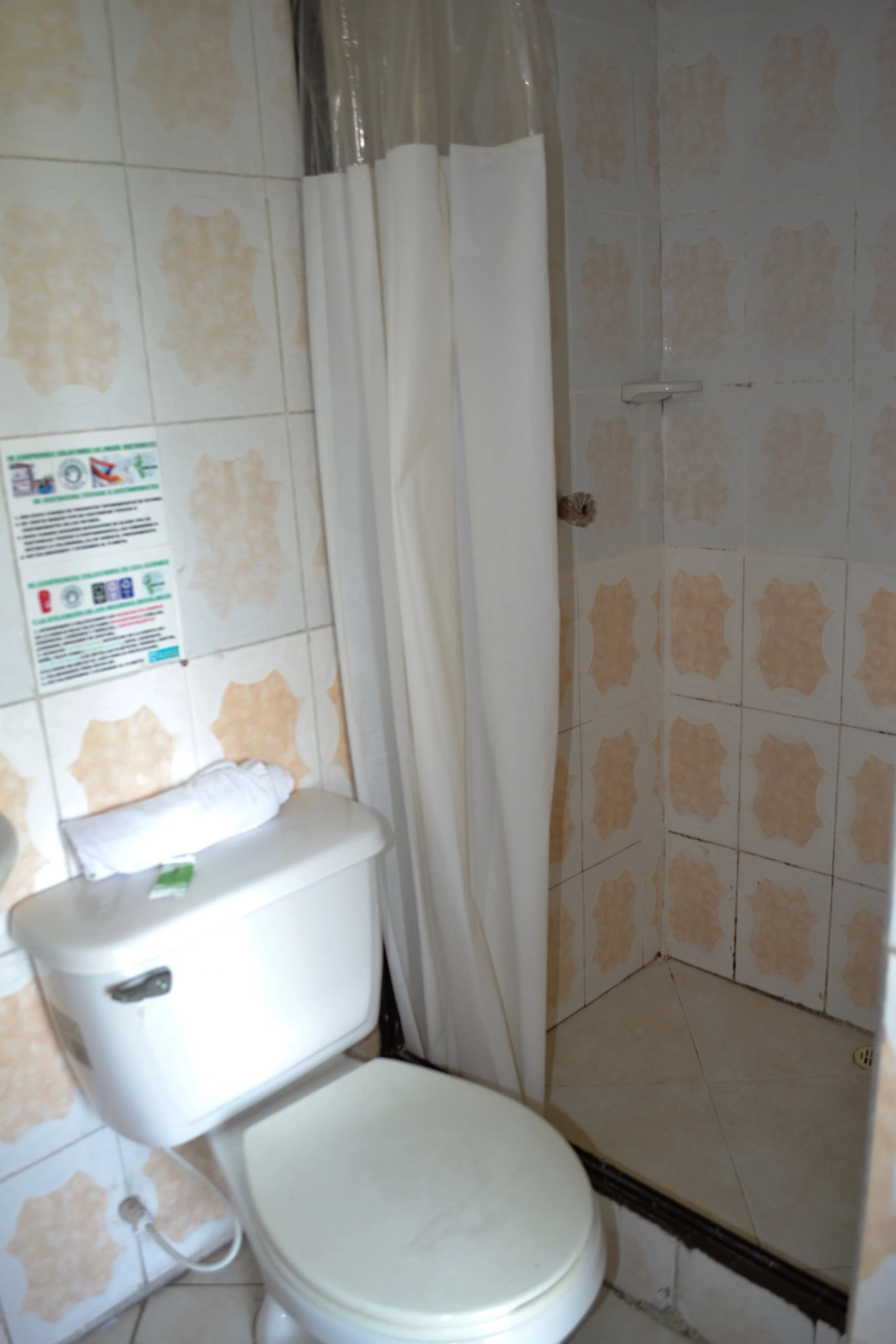 Baño con inodor, ducha con cortina blanca y paredes con azulejos beige y crema.