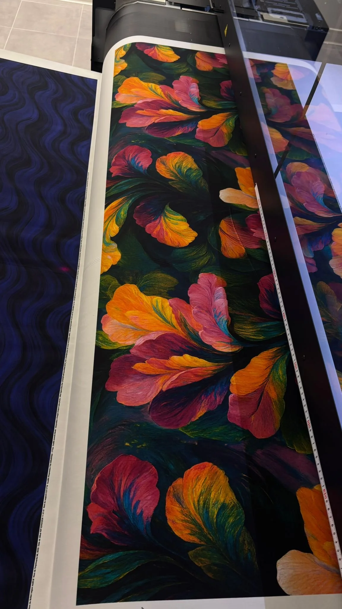 Une imprimante grand format en train d'imprimer une toile avec des fleurs colorées, principalement en nuances de rouge, orange, jaune, vert et bleu.