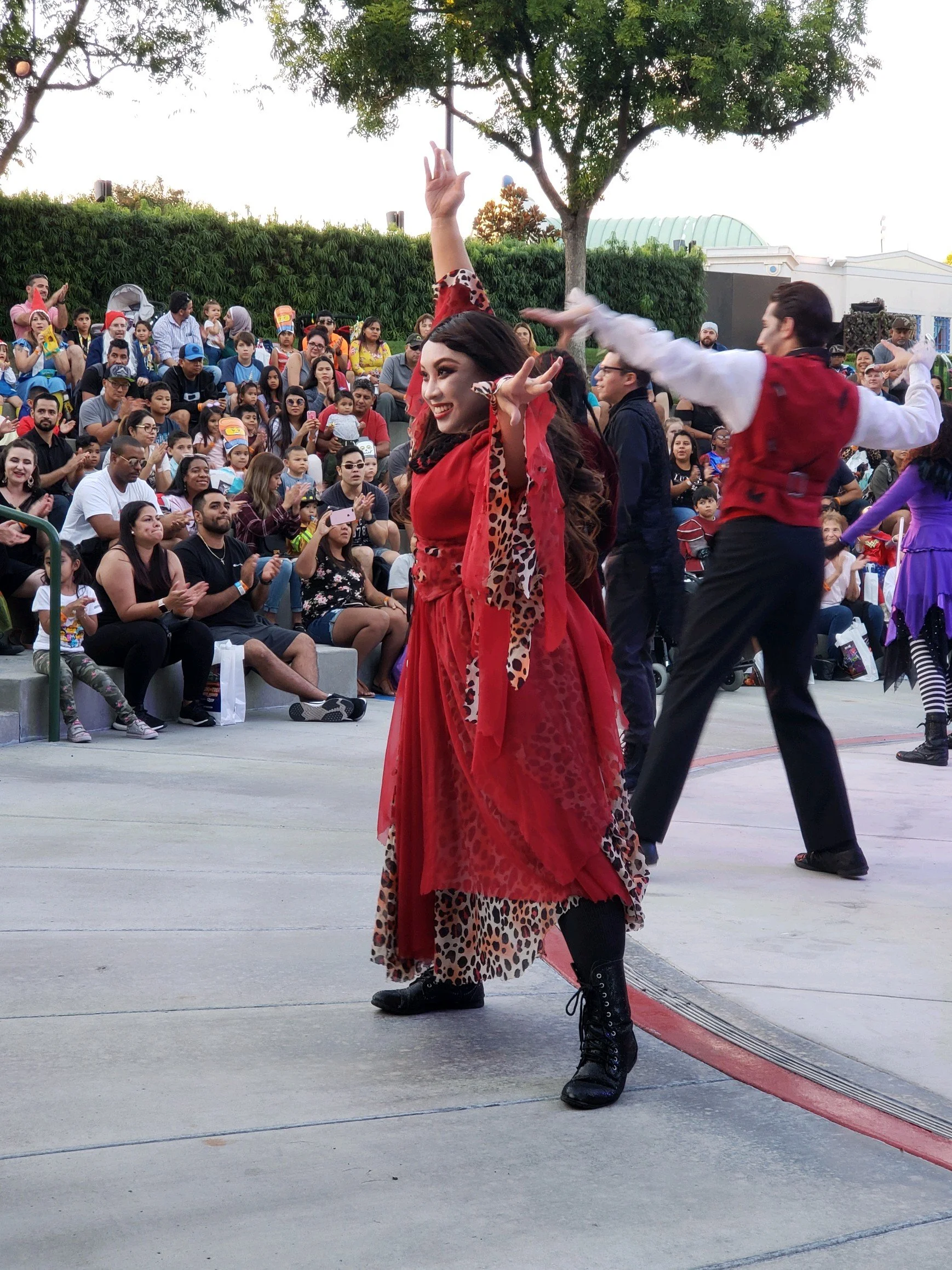Tina Golden performing at Legoland CA. Performer in a red and animal print costume dancing in front of an audience at an outdoor event.