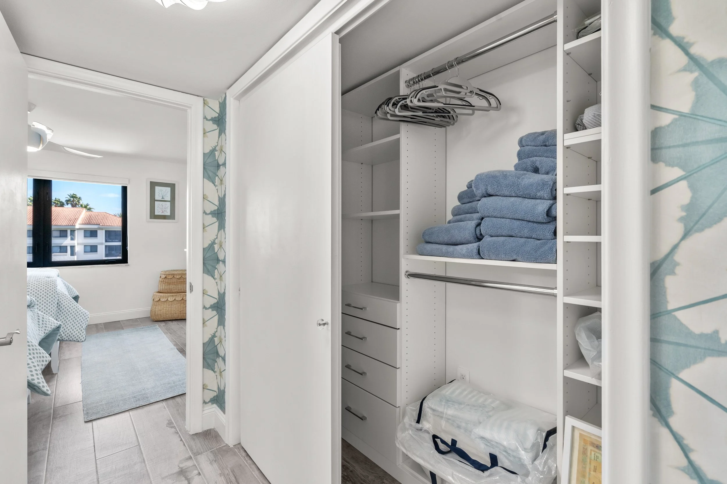 Open closet with folded blue towels, hanging clothes, and shelves for storage in a bedroom.
