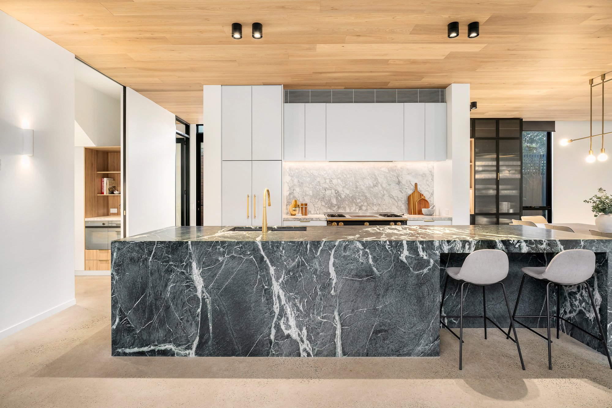Modern kitchen with black marble island, white cabinets, marble backsplash, gold fixtures, and two light-colored chairs