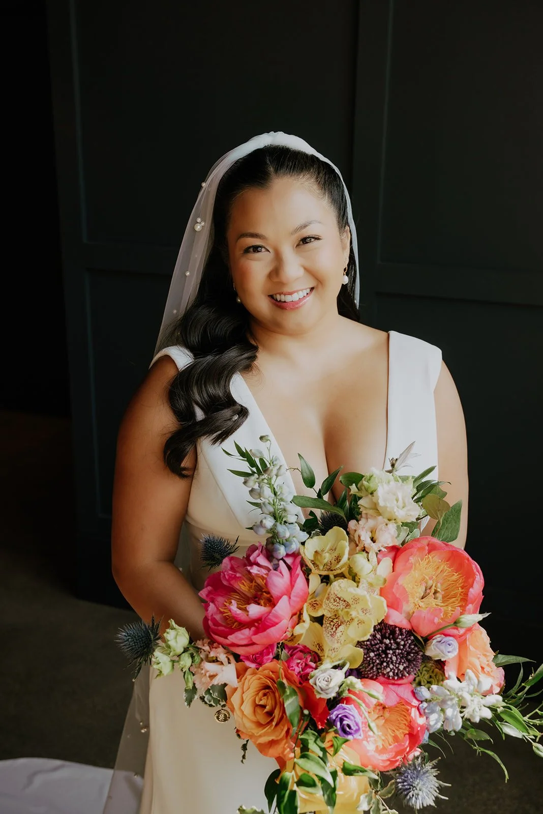 A woman in a white dress holding a large colorful bouquet of flowers, smiling at the camera.
