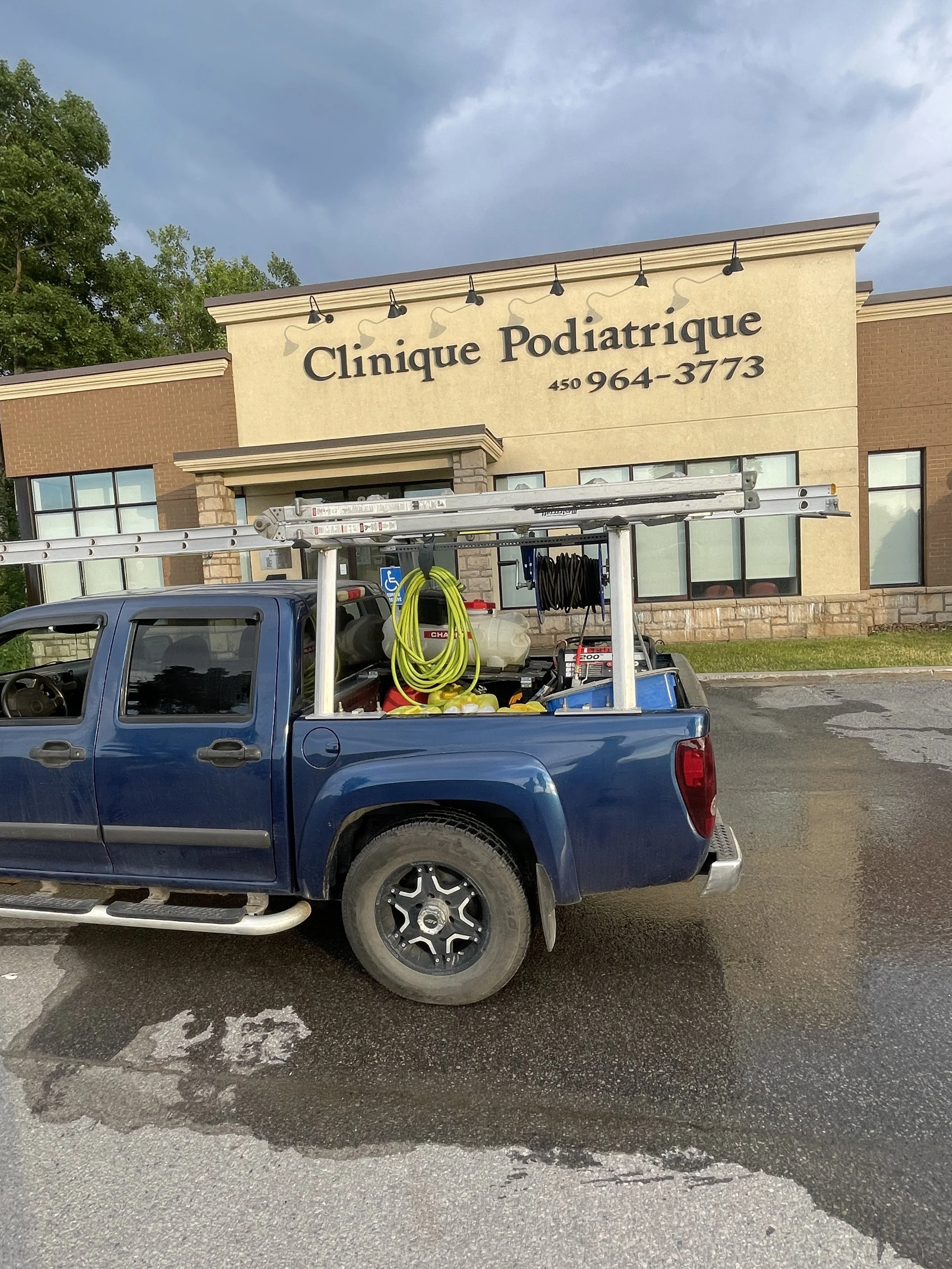 Un camion de service station en stationnement devant une clinique podiatrique. Le camion est chargé d'outils, de tuyaux et d'une échelle.
