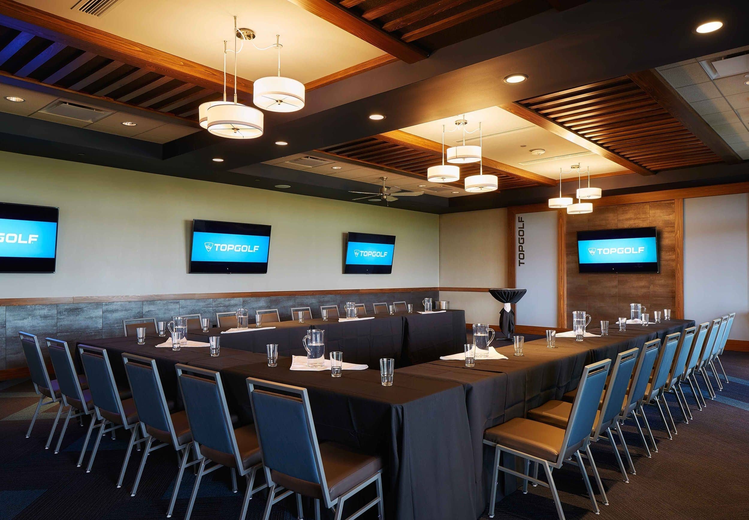 Interior view of a conference and event room featuring a U-shaped table setup, pendant lighting, and wall-mounted screens designed by PARADIGM Structural Engineers.