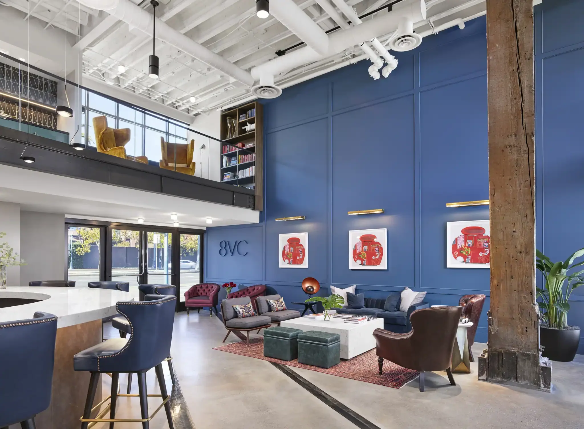 Interior view of the 8VC office featuring a tall blue accent wall, a seating area with armchairs and a coffee table, and an open mezzanine level above.