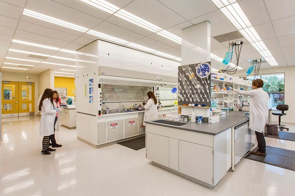 Interior view of the PARADIGM Structural Engineers Bayer CropScience laboratory featuring modern workstations, fume hoods, and researchers in lab coats.