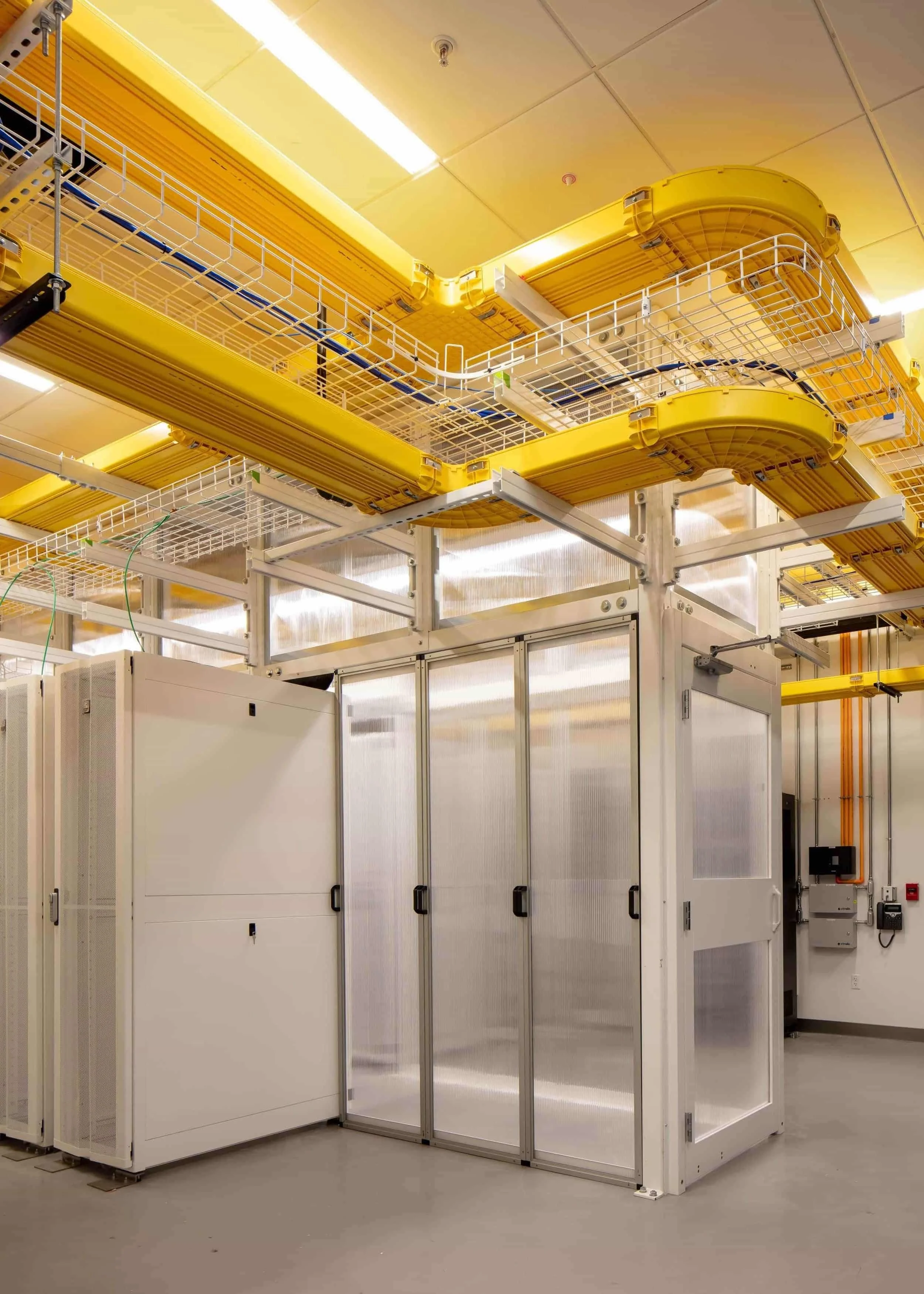 Interior view of the PARADIGM Structural Engineers Ri Cloud data center facility featuring server racks, containment enclosures, and overhead yellow cable trays.