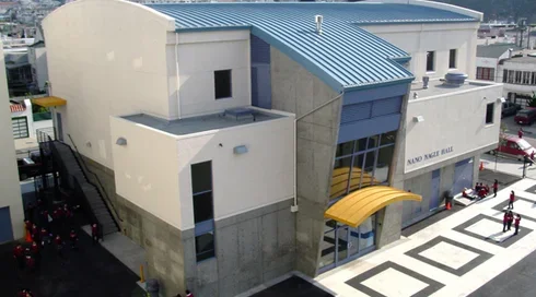 Exterior view of the School of Epiphany gymnasium building featuring a curved blue metal roof, modern concrete facade, and entrance walkway.