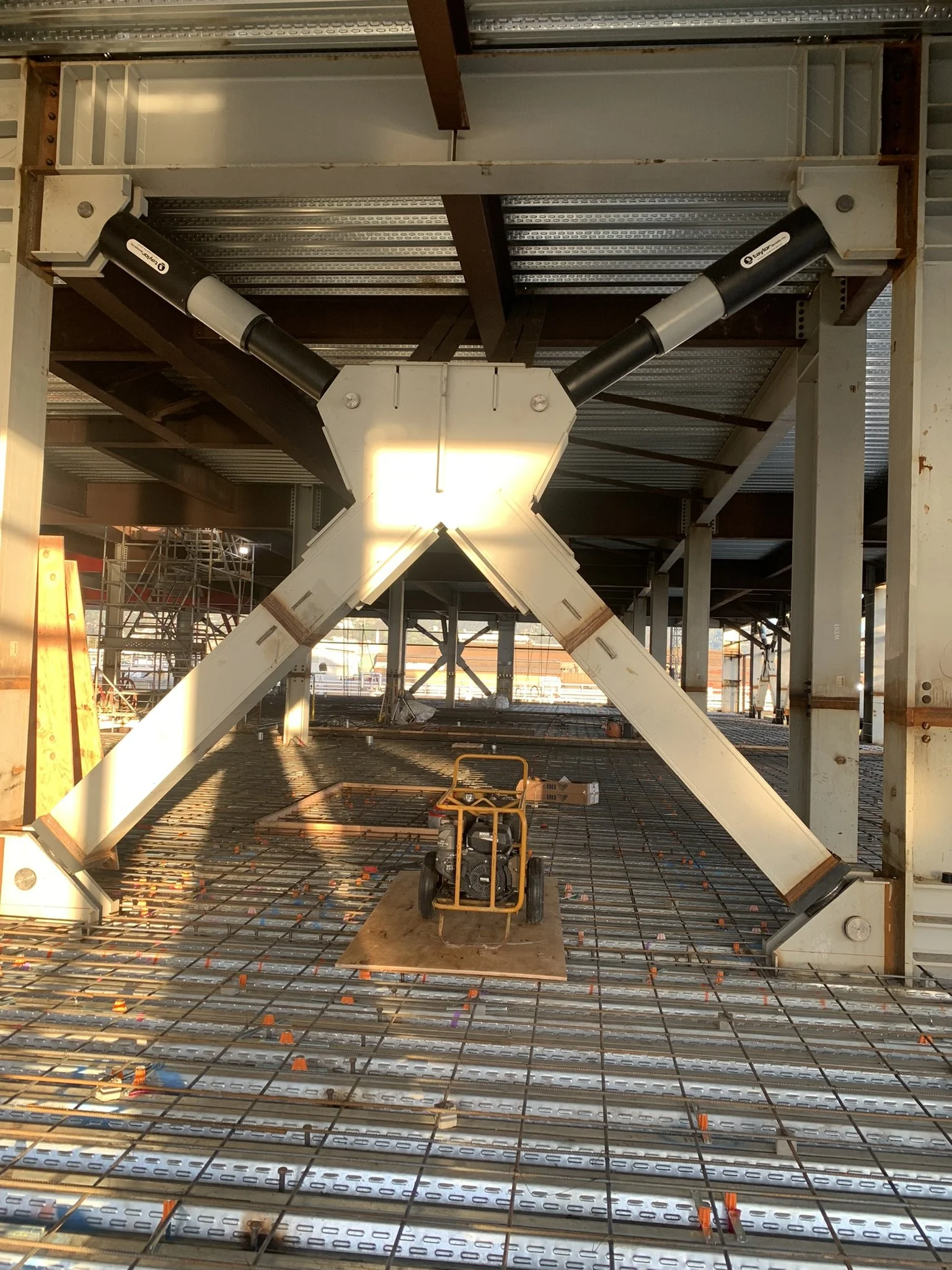 Construction site with structural steel beams and a large robotic arm frame in the center, and scaffolding in the background.