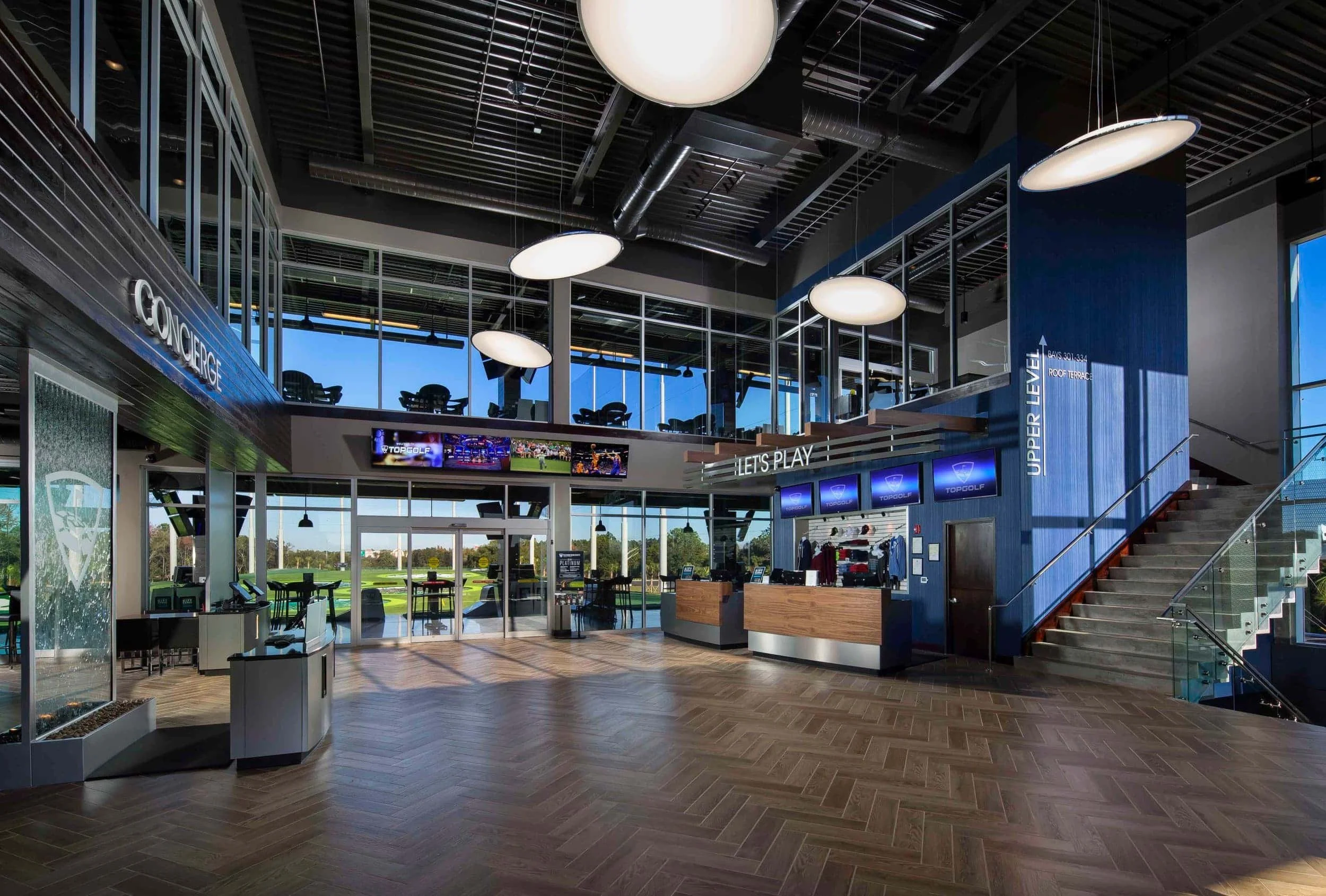 Interior lobby view of the PARADIGM Structural Engineers entertainment and sports facility featuring a grand staircase, reception desks, and open-concept structural design.