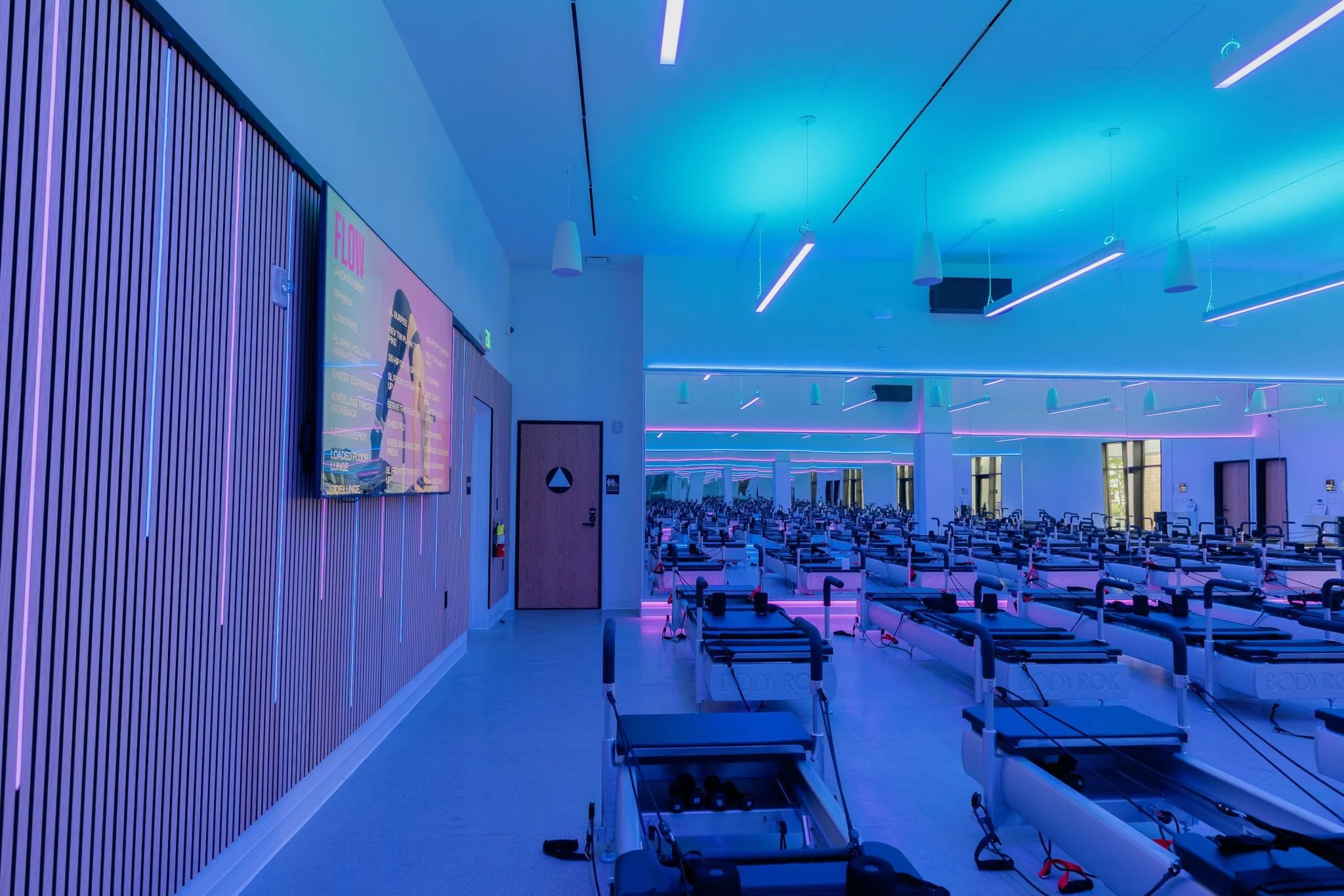 Interior perspective view of the PARADIGM Structural Engineers BODYROK fitness facility featuring slatted wood wall paneling, display screens, and ambient blue lighting across the reformer studio.