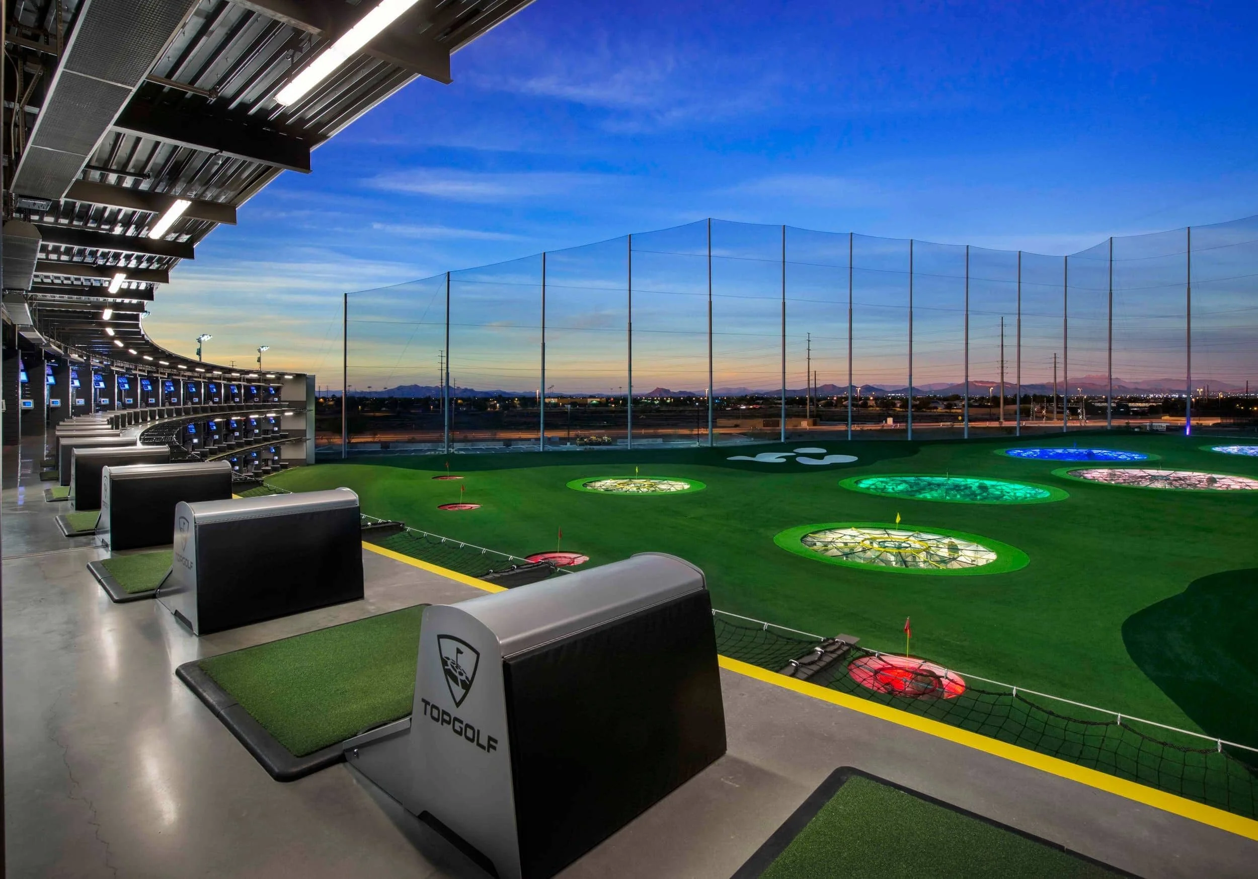Twilight view of a multi-tier driving range facility with hitting bays and illuminated target greens designed by PARADIGM Structural Engineers.