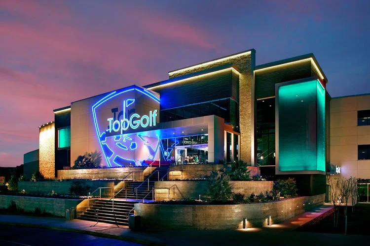 Exterior twilight view of the PARADIGM Structural Engineers entertainment and sports facility featuring illuminated signage, structural framing, and modern architectural lighting.
