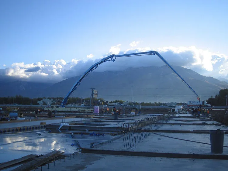 Construction site view for the IKEA project featuring concrete foundation work and heavy machinery with scenic mountains in the background.