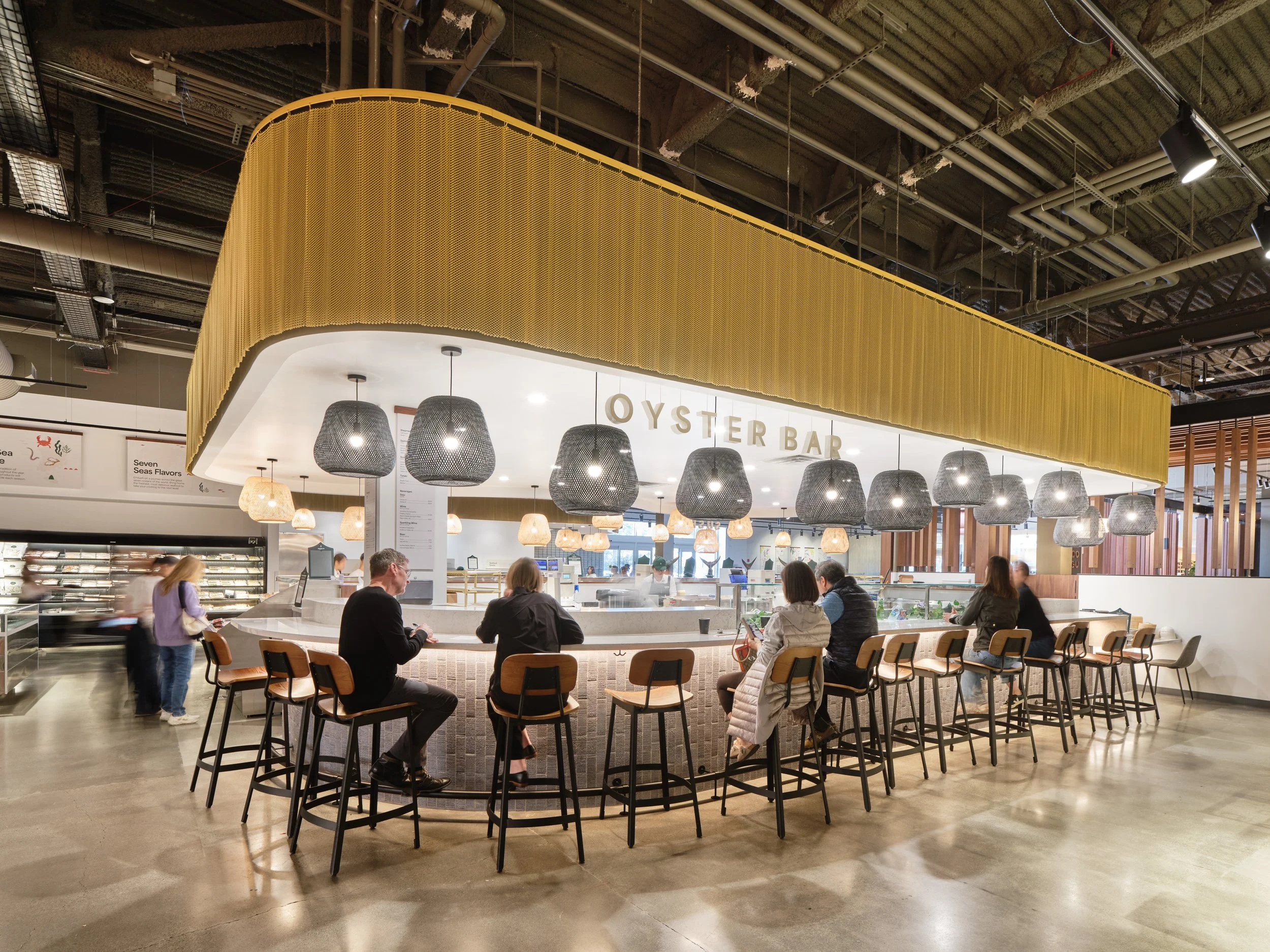 Oyster bar in a modern indoor restaurant with hanging lamps and a curved counter where people are seated.