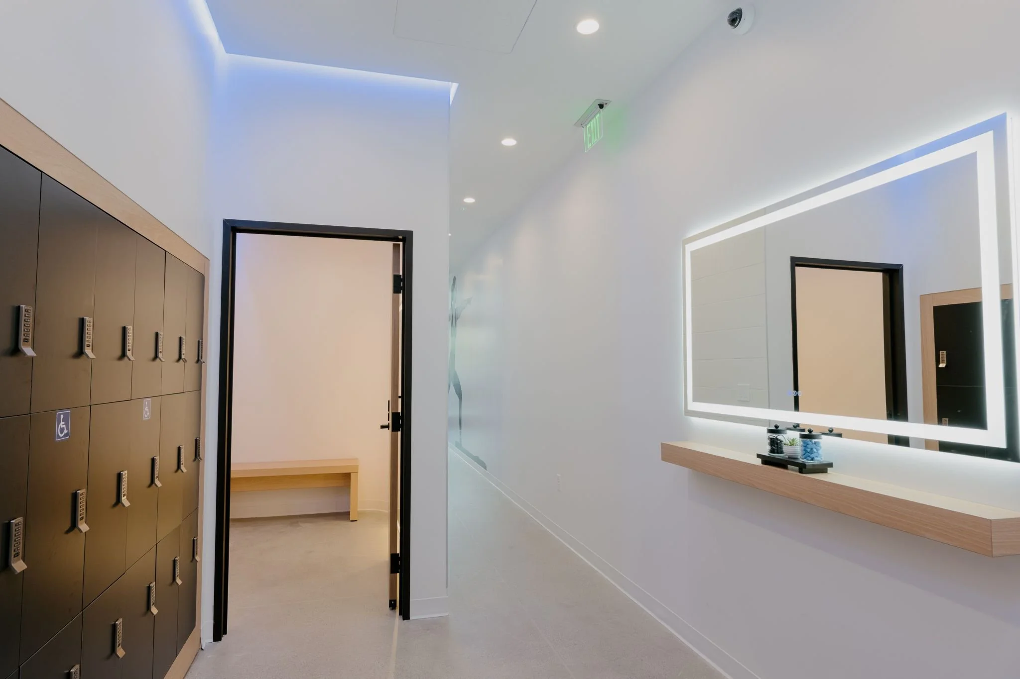 Interior hallway view of the PARADIGM Structural Engineers BODYROK fitness facility featuring modern lockers, a backlit mirror, and a clean white corridor design.