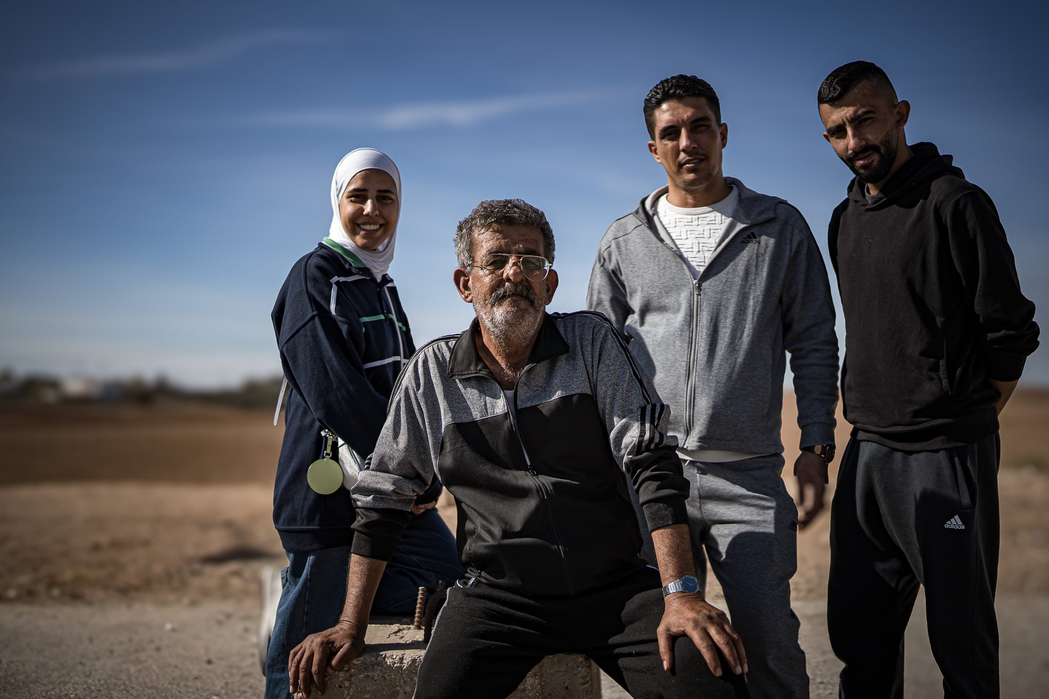 Group of five people standing outdoors on a sunny day, with a flat landscape in the background.