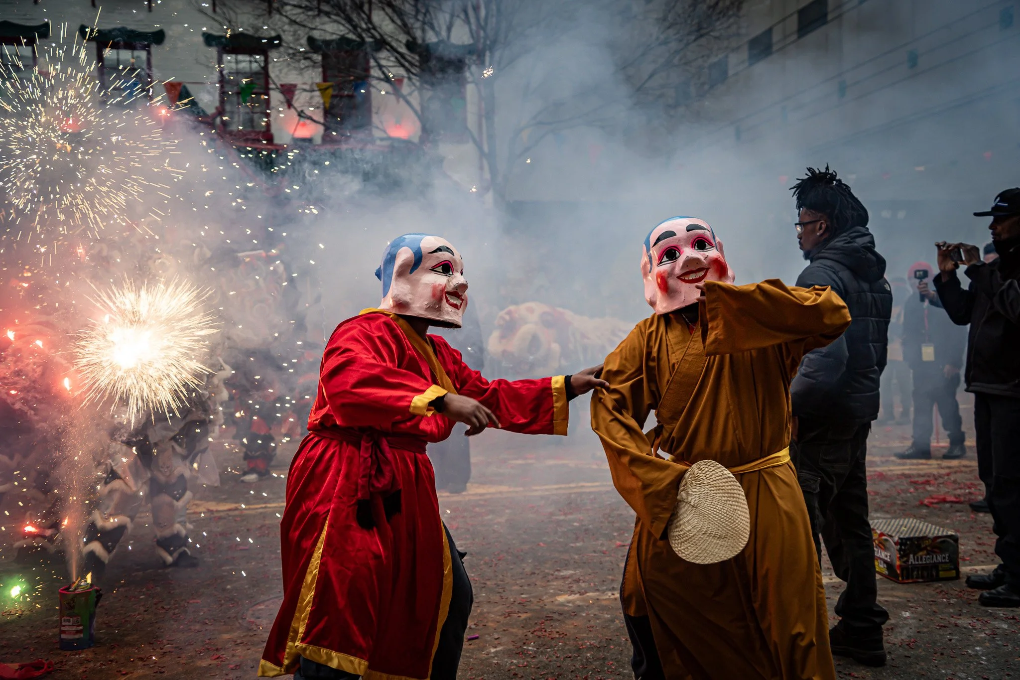 People in traditional costumes with large masks participating in a festival with fireworks and smoke.