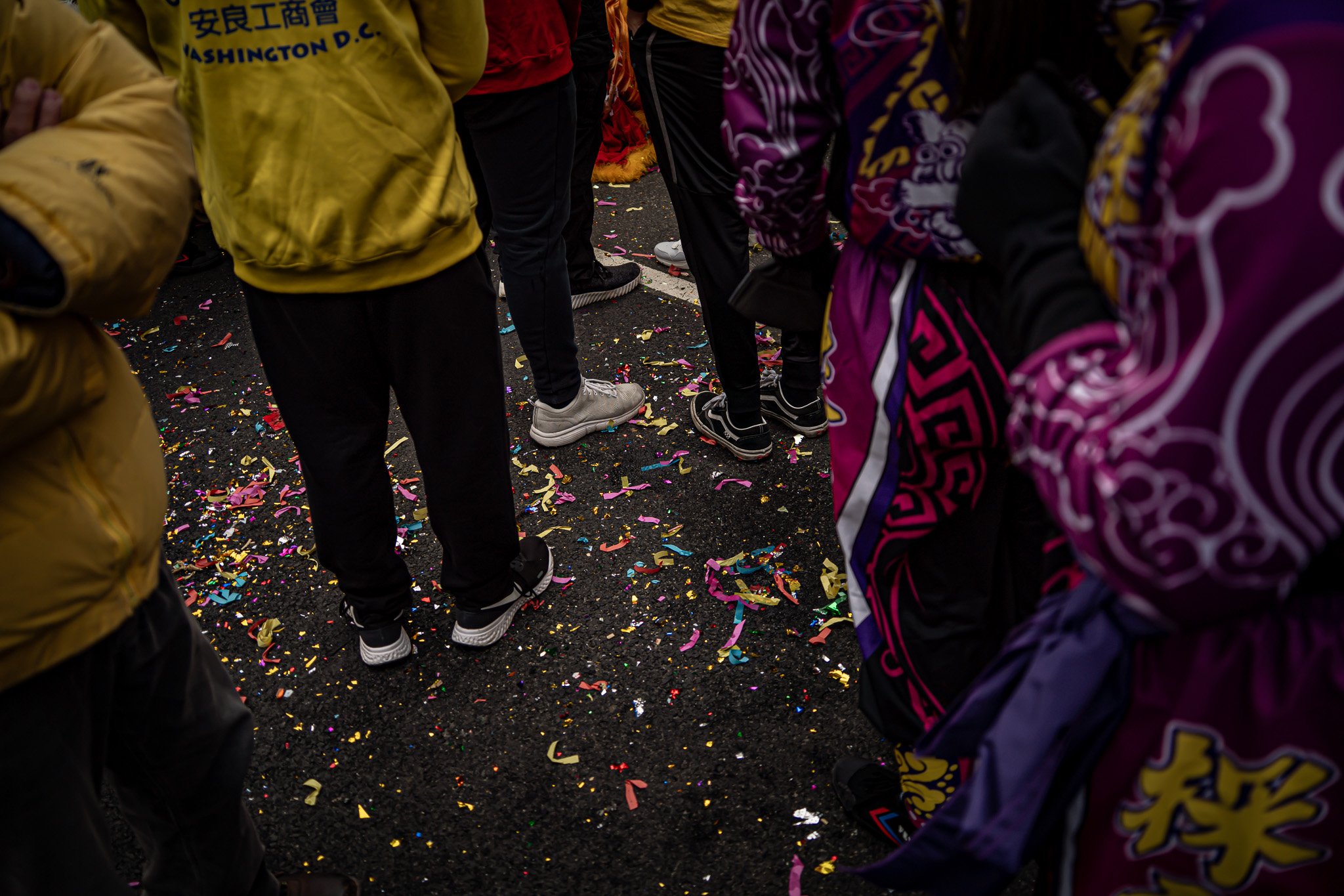 People standing on a street with colorful confetti scattered on the ground, dressed in bright and patterned jackets, celebrating a festive occasion.