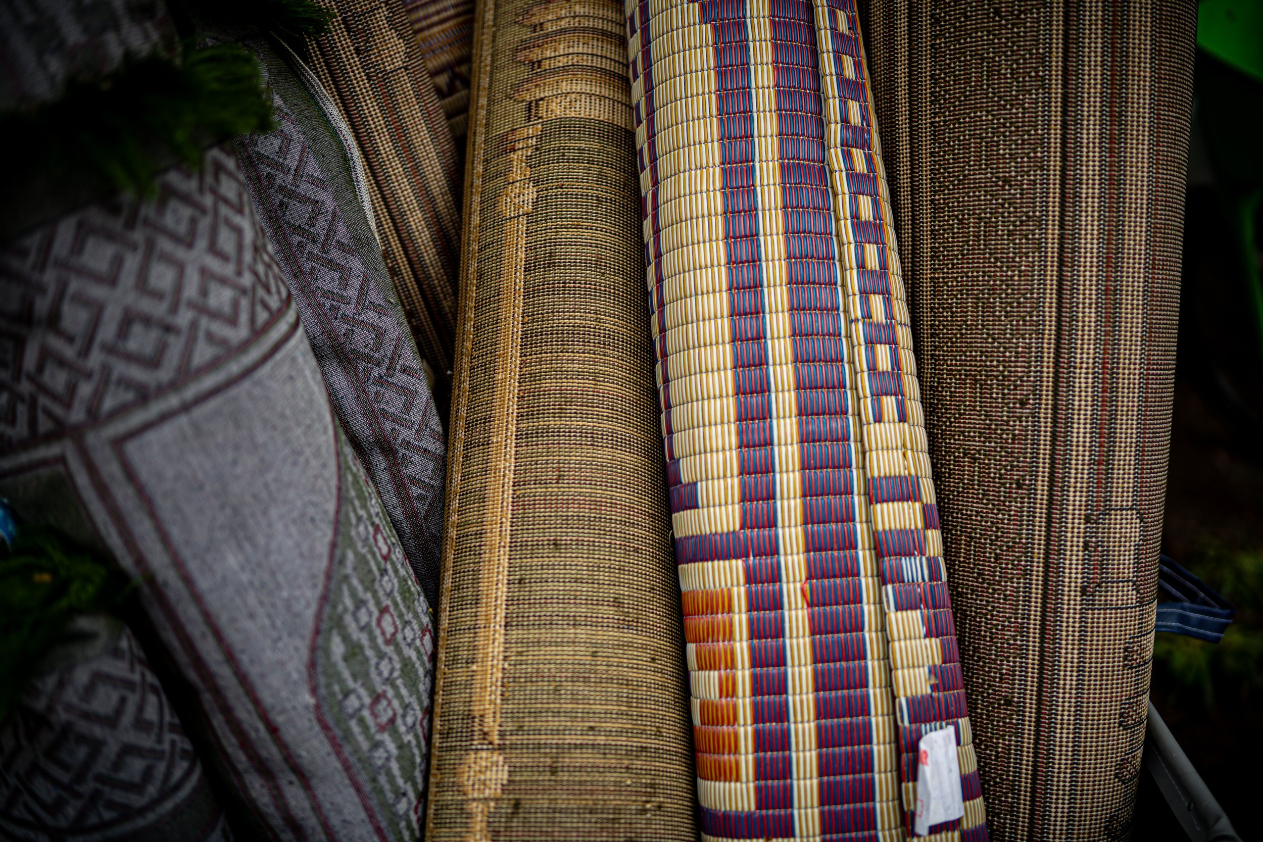 Various rolled and woven mats with intricate patterns and natural colors displayed vertically.