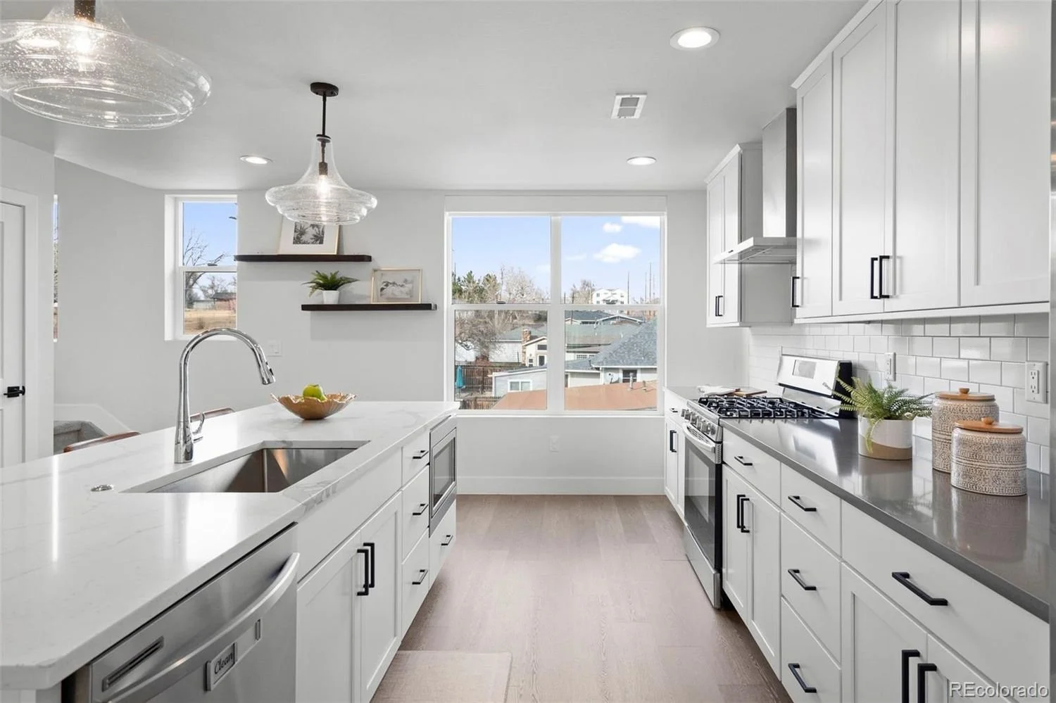 Modern white kitchen with island, large window, and white cabinetry