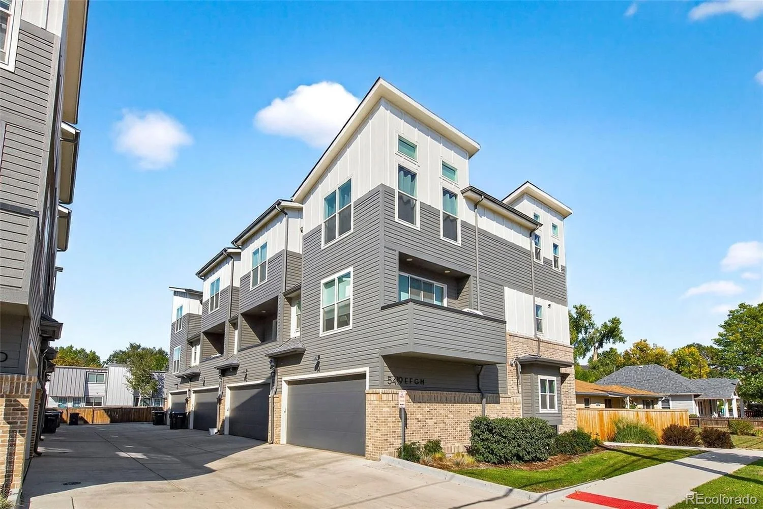 Multi-story modern apartment building with garages in the front under a clear blue sky.