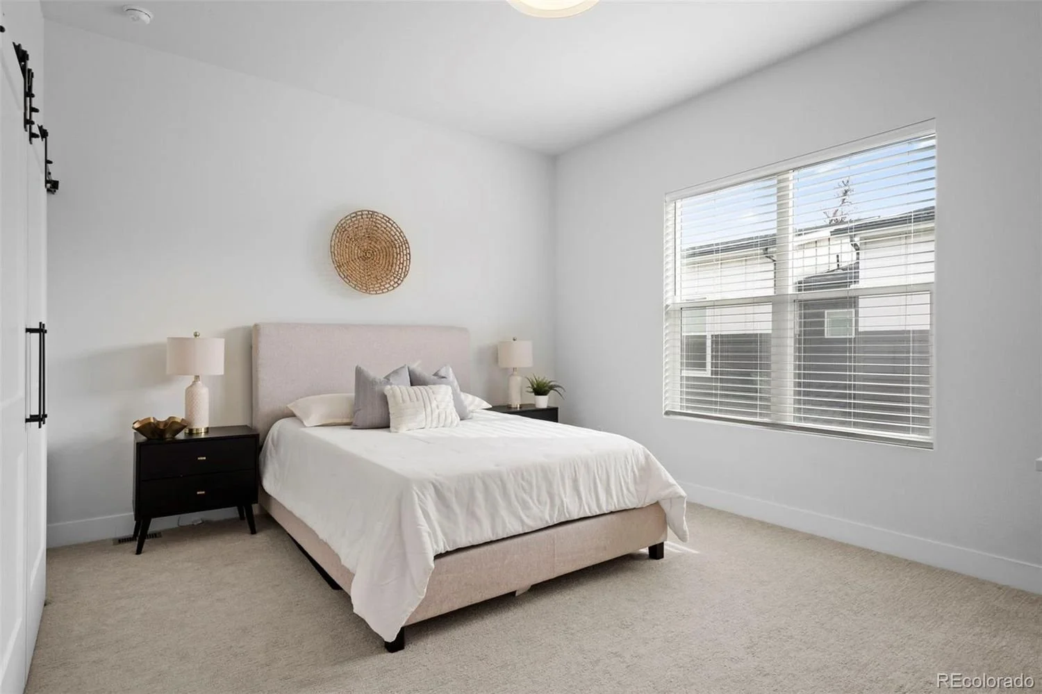 A bedroom with a bed, two nightstands with lamps, a window with blinds, and wall decor.