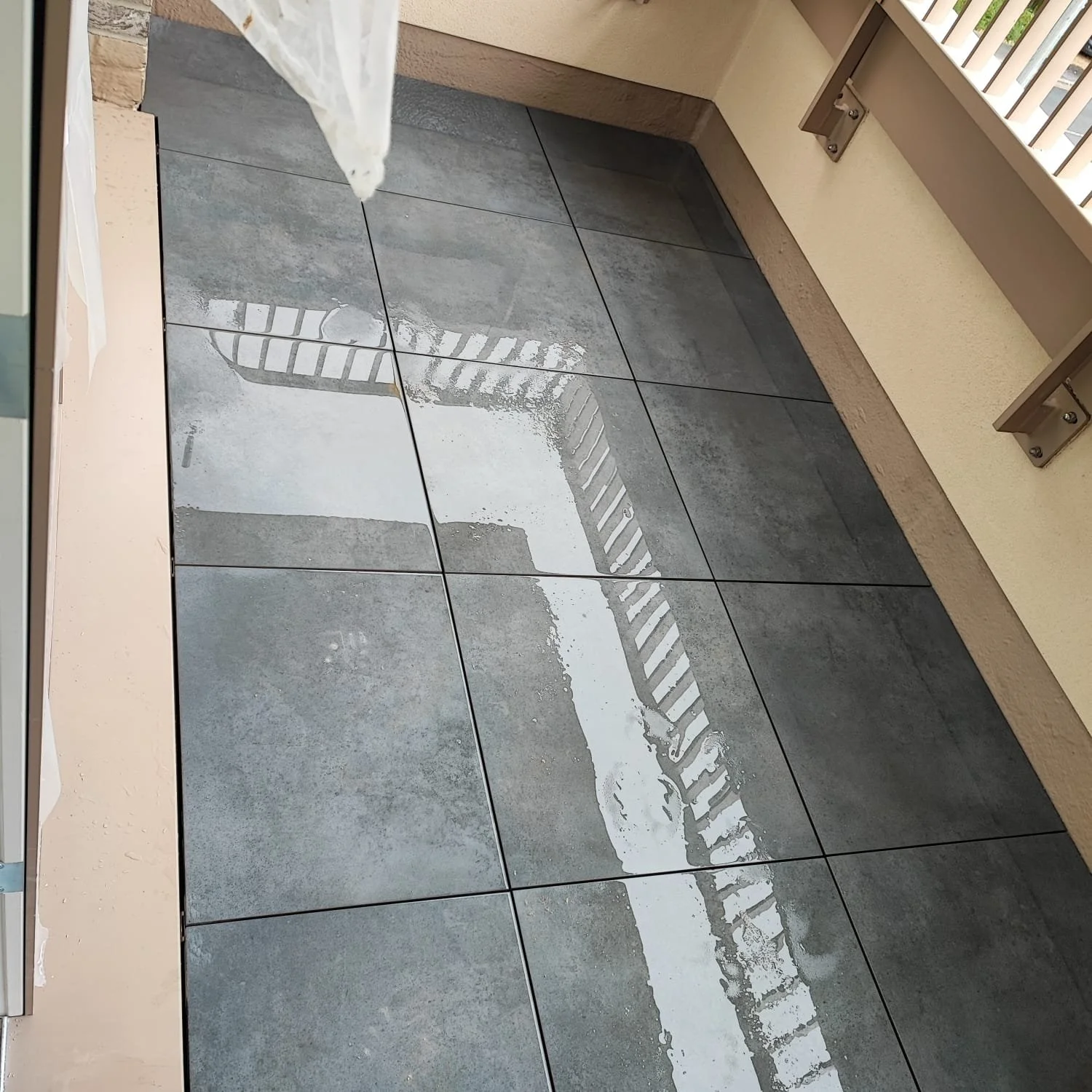 Wet tile floor with reflections of a railing and a wall.