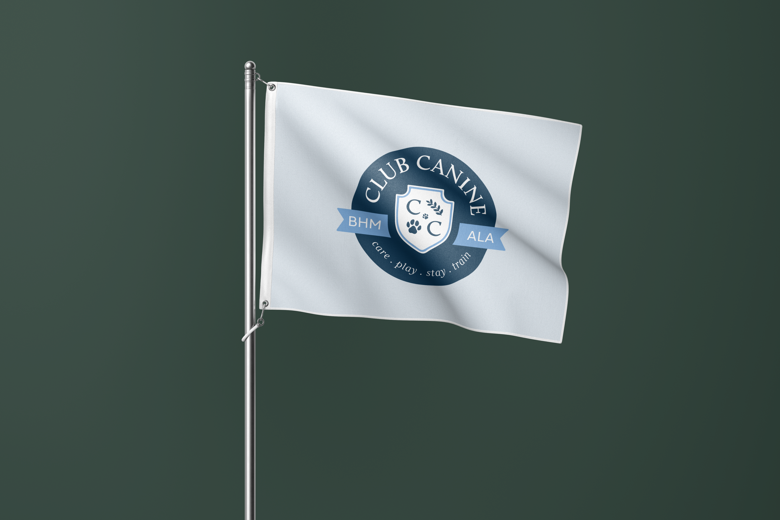 A white flag with a blue logo and text, attached to a silver flagpole, flying against a dark green background. The logo reads 'Club Canine' with paw prints and a shield emblem, and the text around the logo says 'care. play. stay. train'.