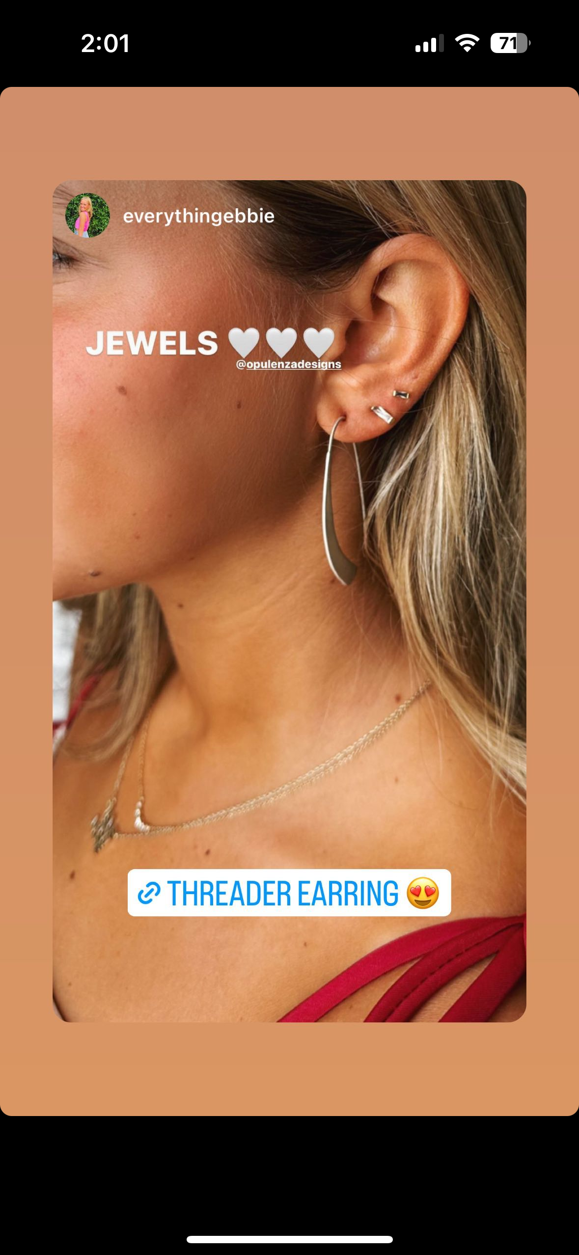 Close-up of a woman's ear with multiple earrings, including a chain threaded earring, necklace, and a red top strap visible.