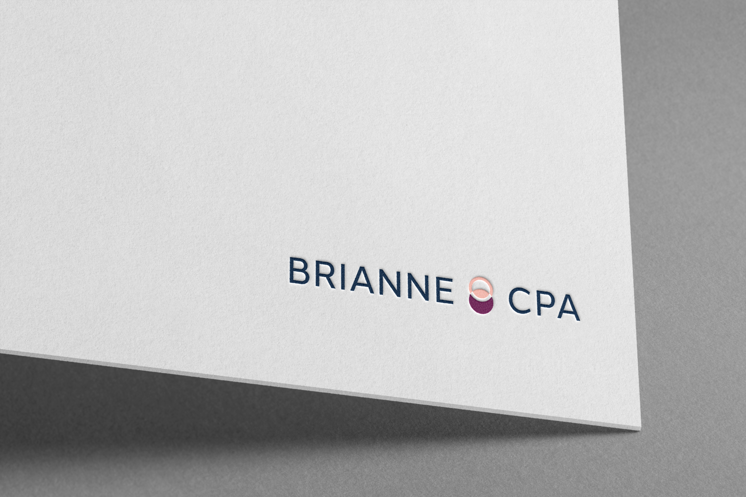 Close-up of a white surface with partial text reading 'BRIANNE' and 'CPA', with a small graphic of two linked circles in pink and purple beneath the text, on a dark background.